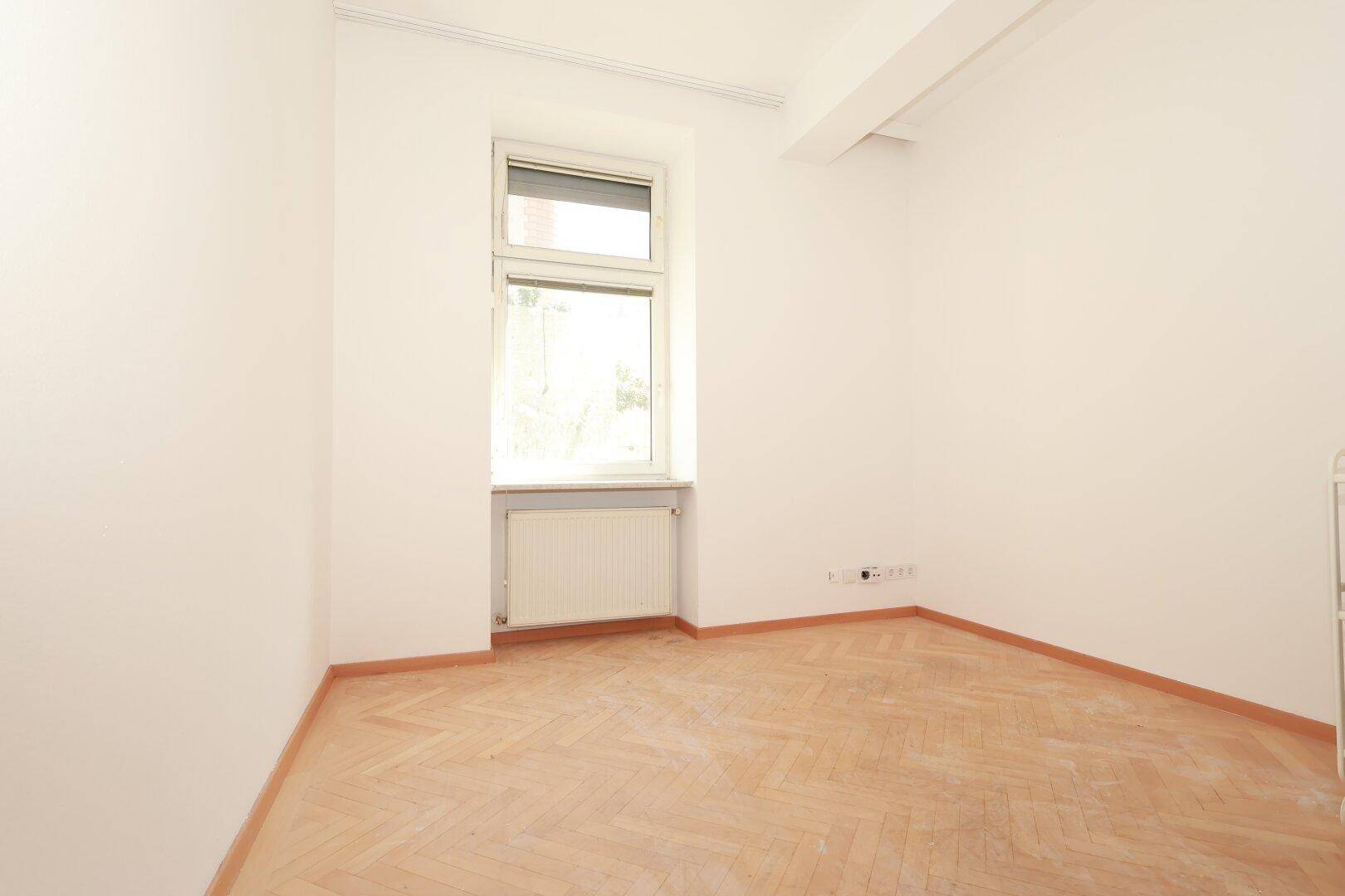 Ruhiges Schlafzimmer mit hellem Fischgrätparkett, weißen Wänden und einem Fenster mit Rollladen.