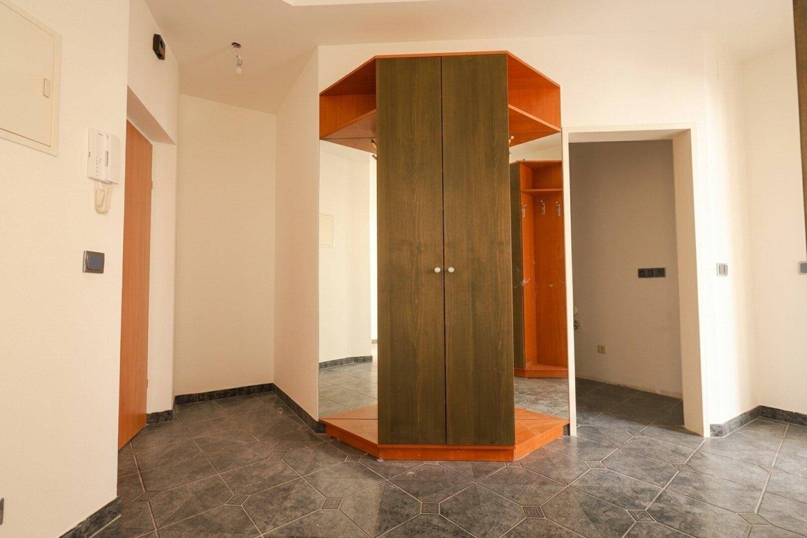 Eingangsbereich mit dunklen Fliesen und einem integrierten Holzschrank mit Spiegelfronten.