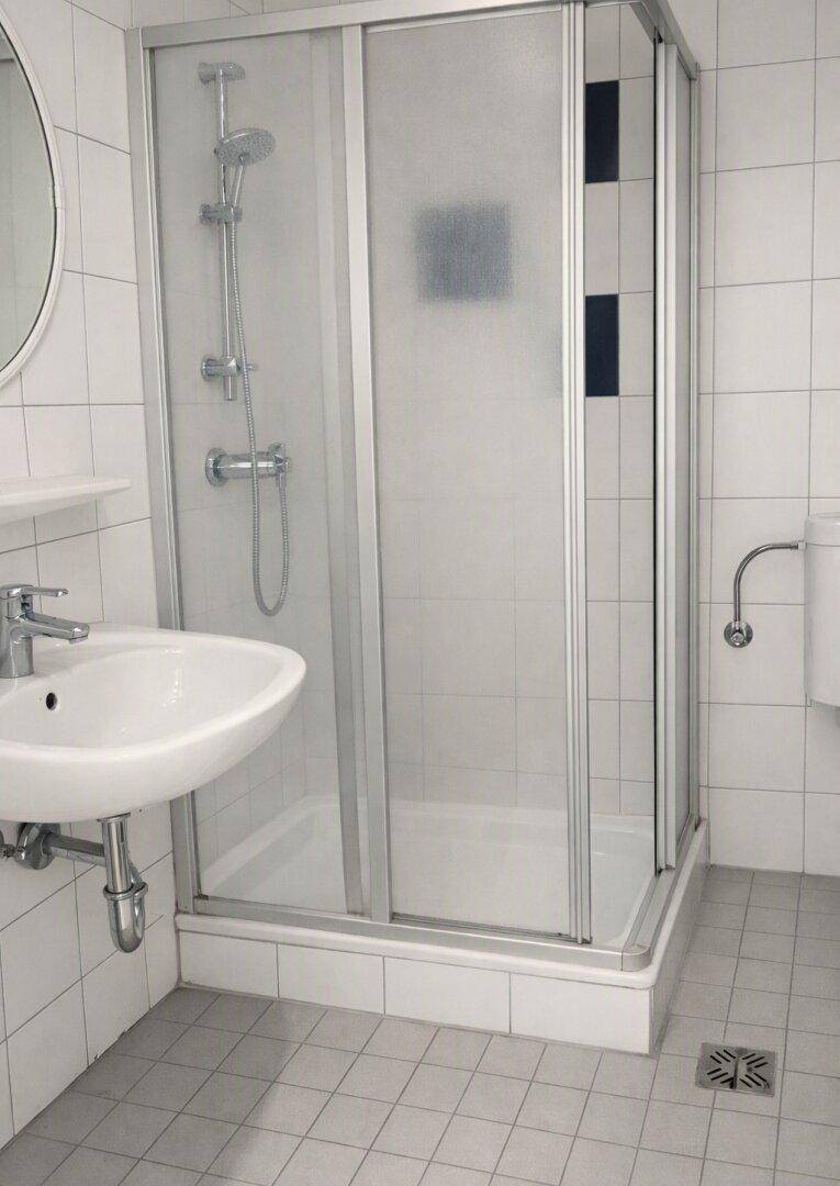 Funktionales Badezimmer mit Duschkabine, Waschbecken und hellen Fliesen.