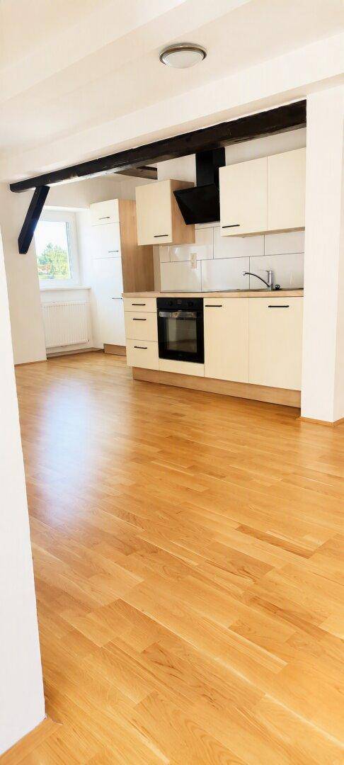 Offener Küchenbereich mit hellem Parkettboden und sichtbaren Holzbalken an der Decke.
