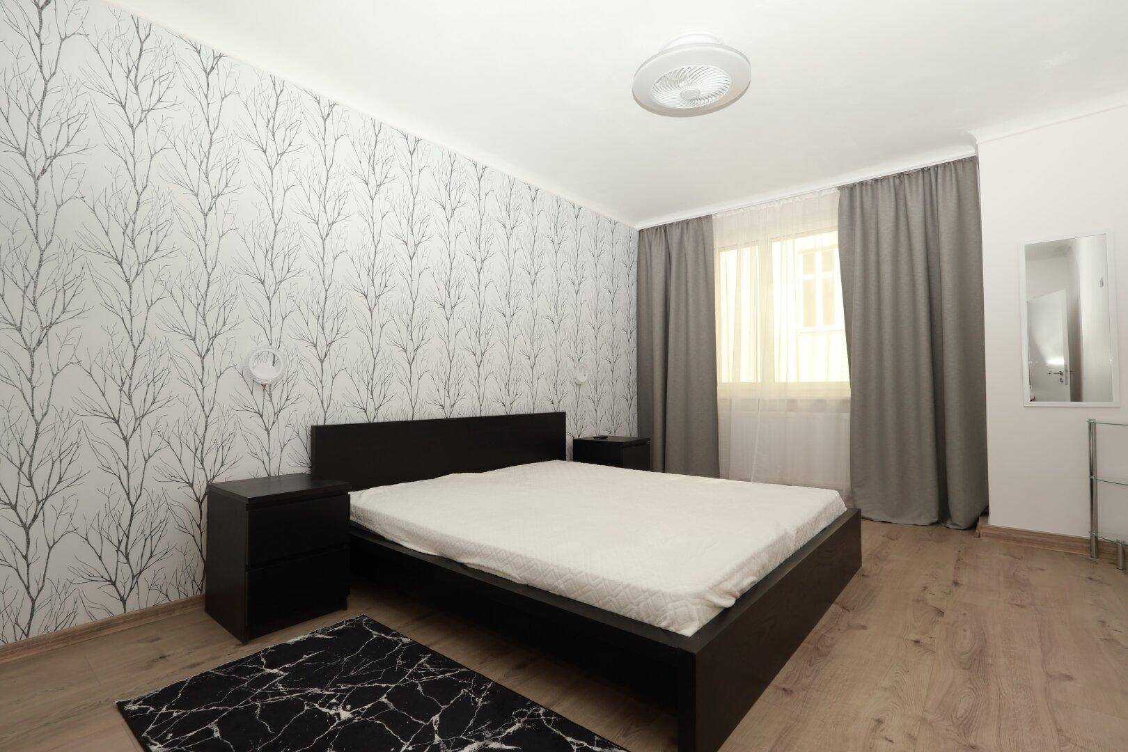 Gemütliches Schlafzimmer mit modernem Bett, Nachttischen und auffälliger Tapete, heller Laminatboden.