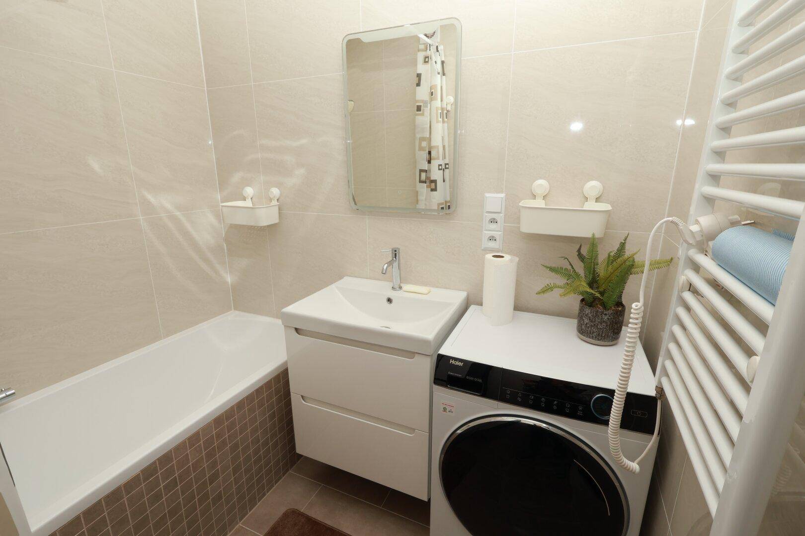 Modernes Badezimmer mit Badewanne, Waschbecken und Waschmaschine, hell gefliest.