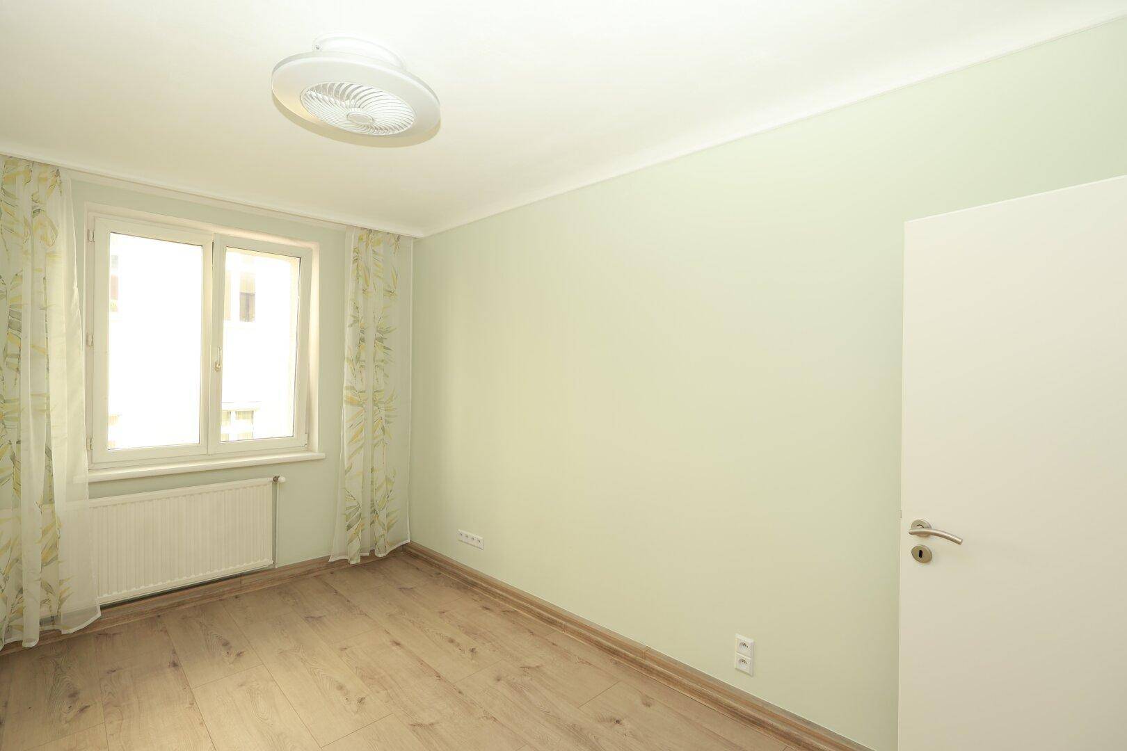Helles Zimmer mit hellgrünen Wänden und Laminatboden, ideal als Kinder- oder Gästezimmer.