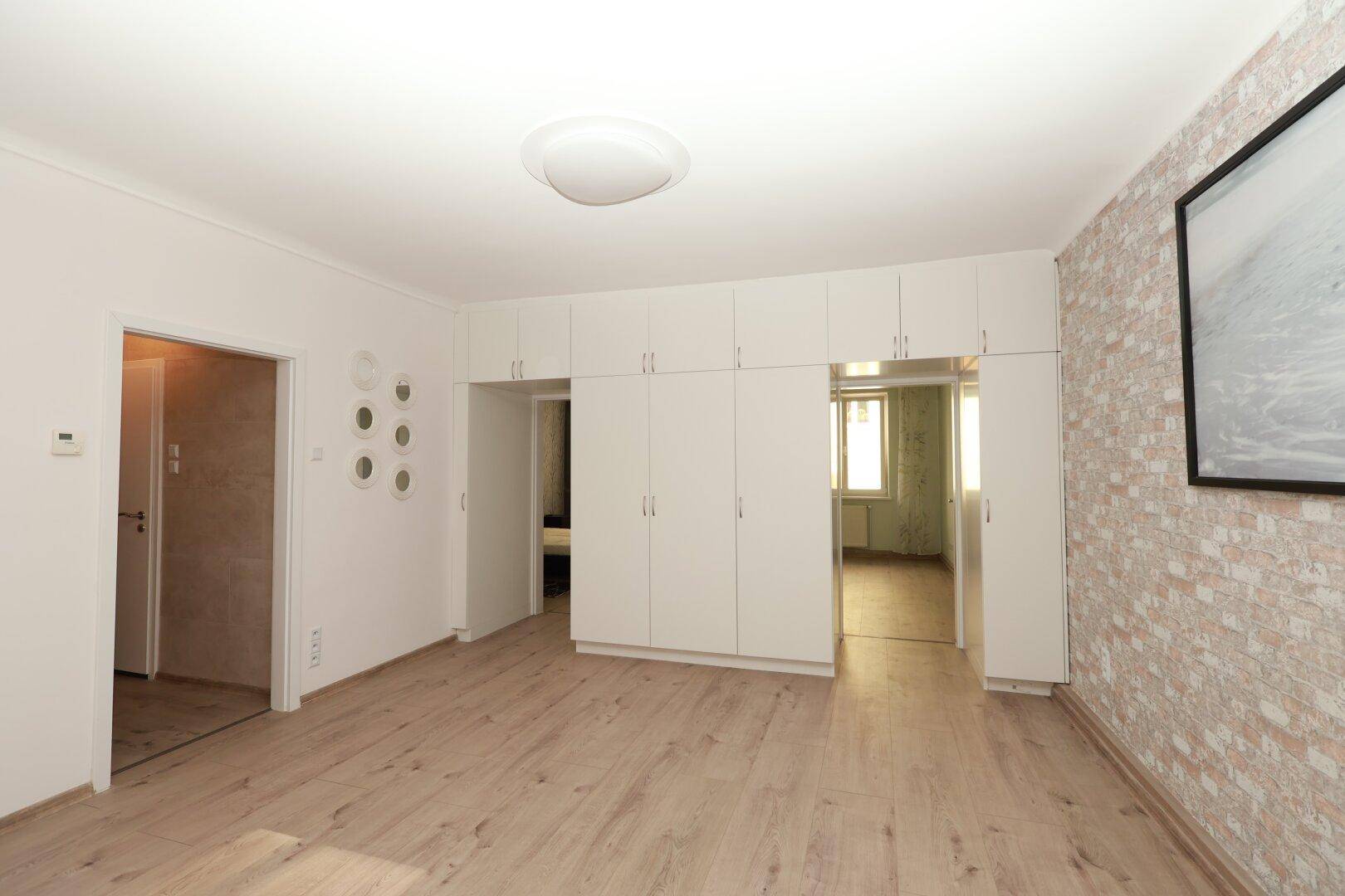 Geräumiges Zimmer mit Einbauschränken und Zugang zu weiteren Räumen, heller Laminatboden.
