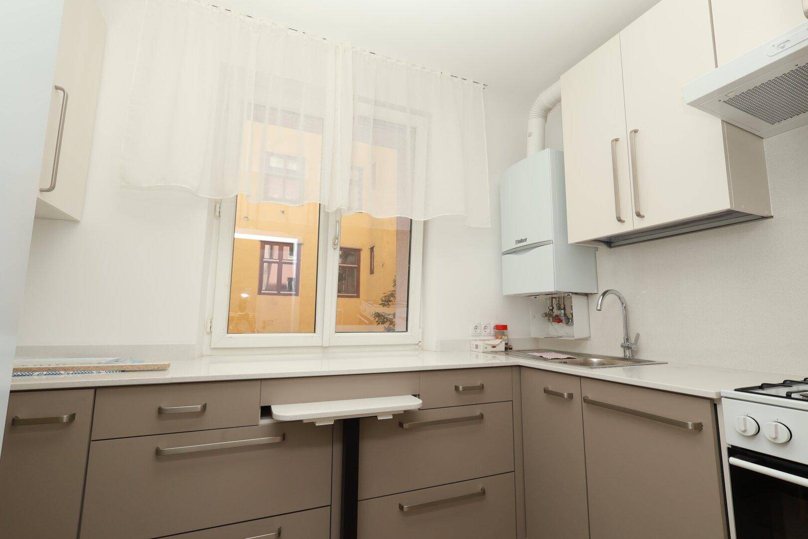 Funktionale Küche mit beigen Schränken, Spüle und Gasherd, mit Fenster zum Innenhof.