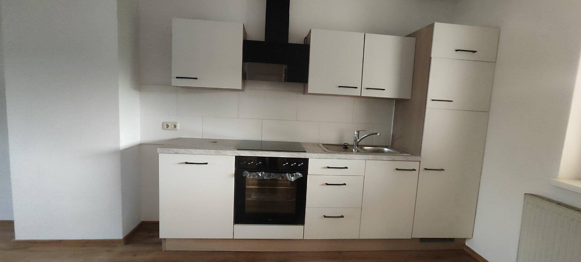 Moderne Einbauküche mit hellen Schränken, integriertem Backofen und Kochfeld sowie einer Dunstabzugshaube.