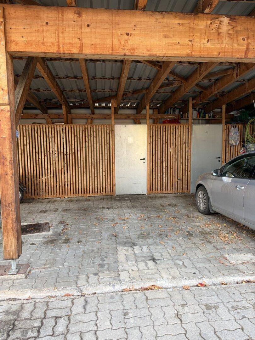 Überdachter Stellplatz oder Carport mit Holzkonstruktion und gepflastertem Boden.