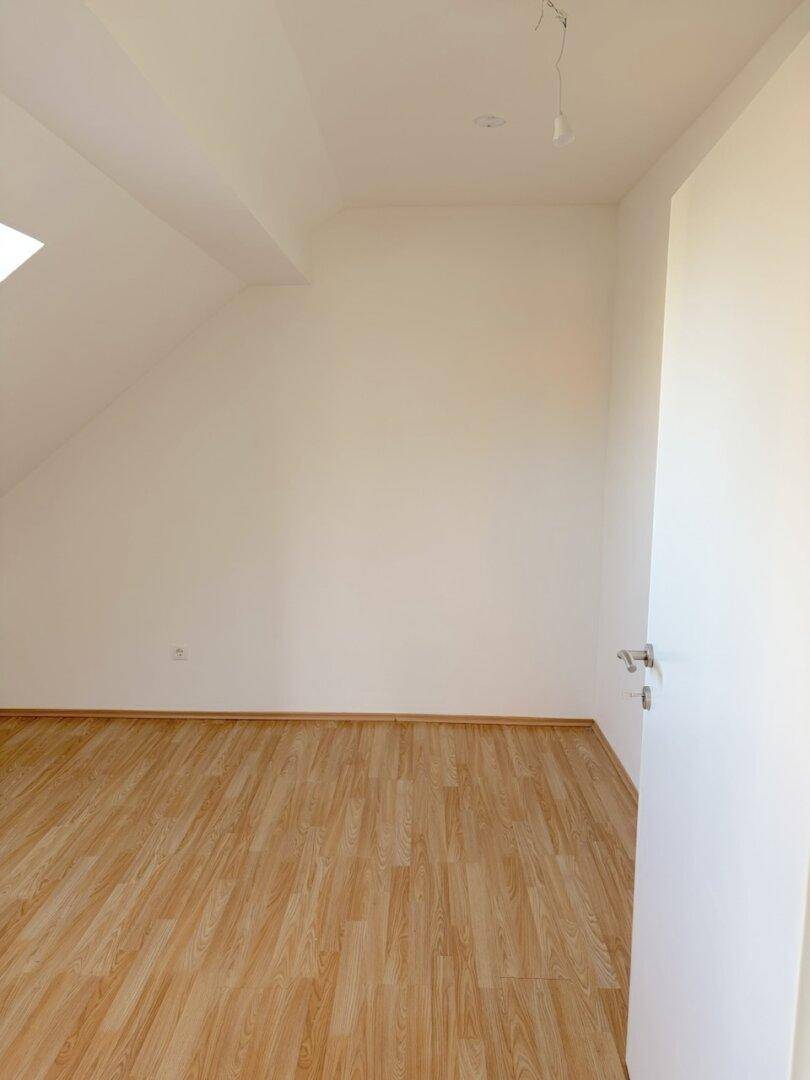 Geräumiger Raum im Dachgeschoss mit Parkettboden, Dachschräge und einem Dachfenster.