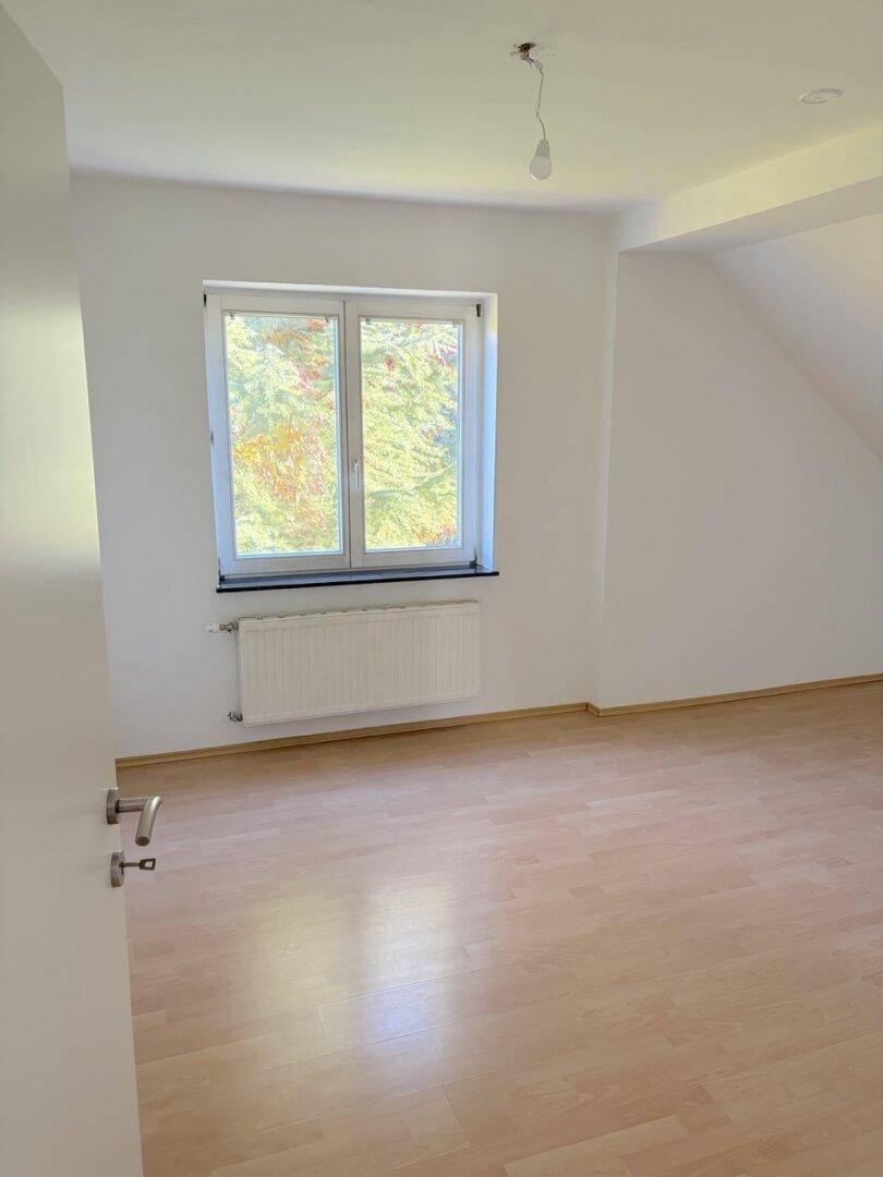 Helles Schlafzimmer mit Dachschräge, Parkettboden und Fenster mit Blick ins Grüne.