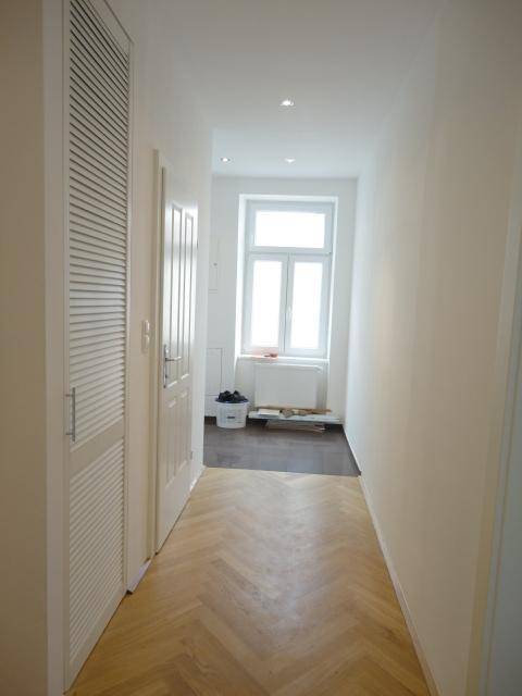 Heller Flur mit Fischgrätparkett, weißen Wänden und integrierten Schränken, der zu einem Fenster führt.