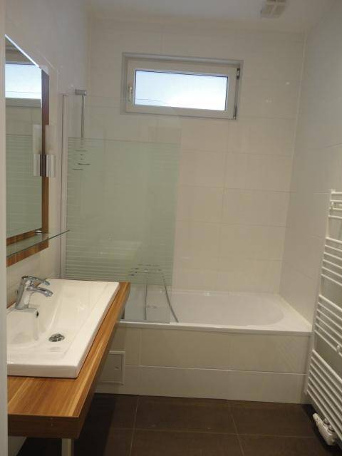 Modernes Badezimmer mit Badewanne, Holzwaschtisch, Spiegel und einem kleinen Fenster für Tageslicht.