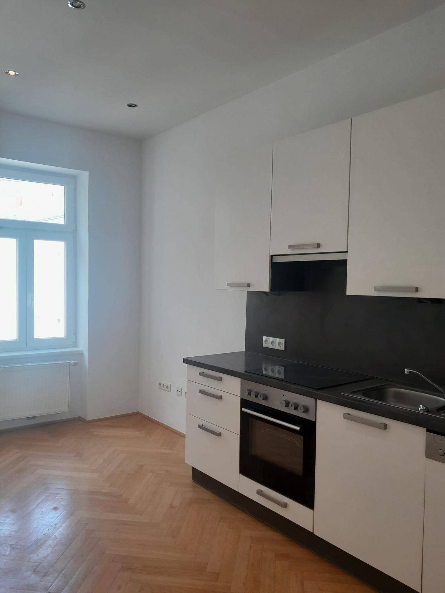 Küche mit weißen Schränken, schwarzer Arbeitsplatte und integrierten Geräten, beleuchtet durch ein Fenster.