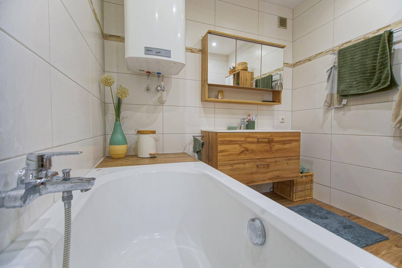 Badezimmer mit Badewanne, Holzwaschtisch, Spiegelschrank und Warmwasserboiler.