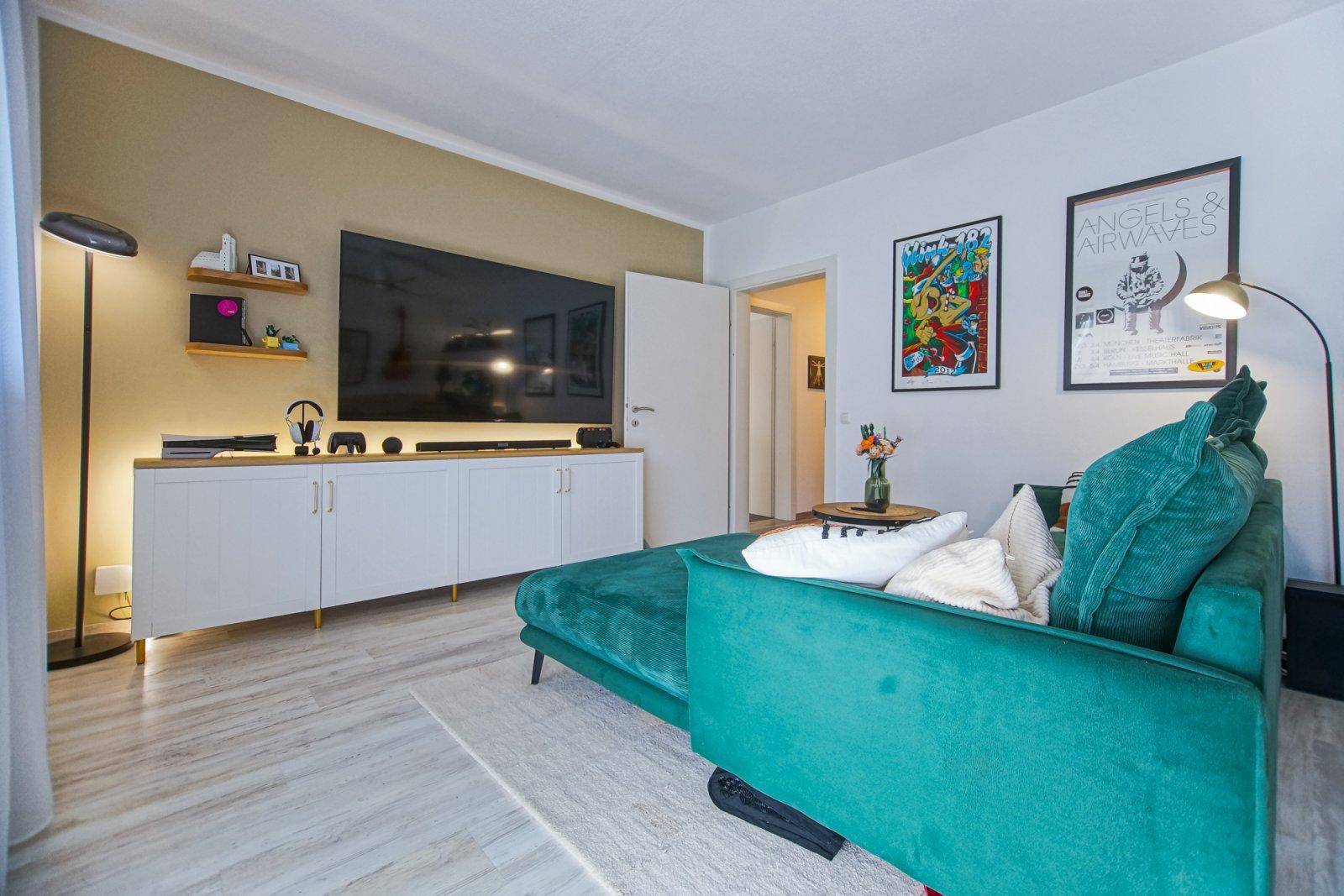 Modernes Wohnzimmer mit grüner Couch, großem Fernseher und stilvollen Wandbildern.