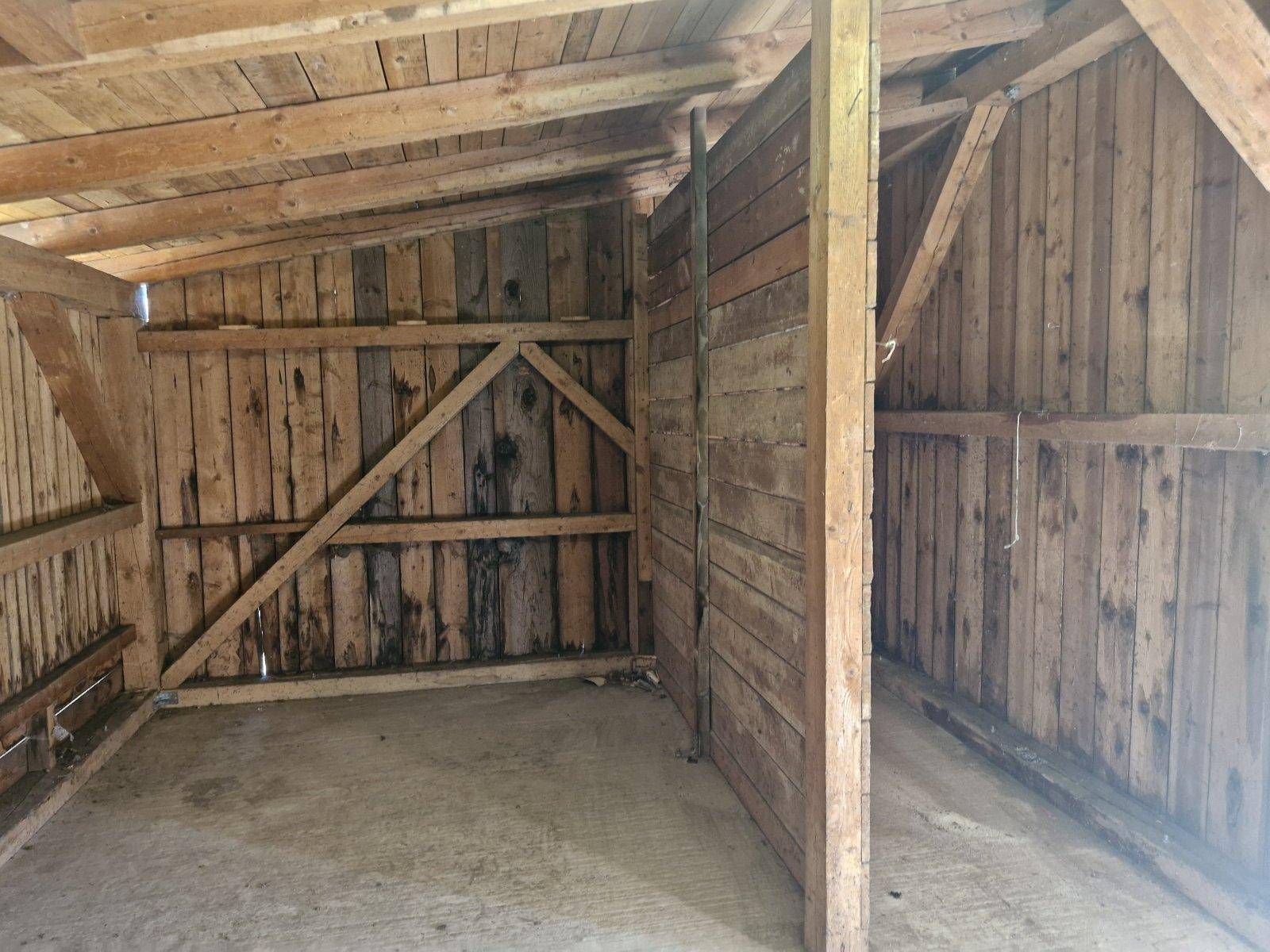 Innenansicht einer Holzkonstruktion, möglicherweise eine Garage oder ein Schuppen, mit sichtbaren Balken.