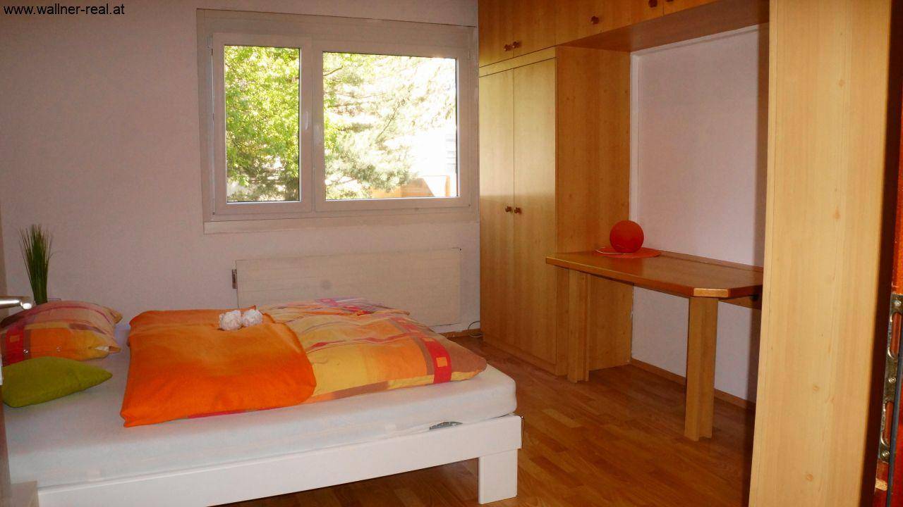 Schlafzimmer mit Holzfußboden, Fenster und praktischen Einbauschränken mit Schreibtisch.