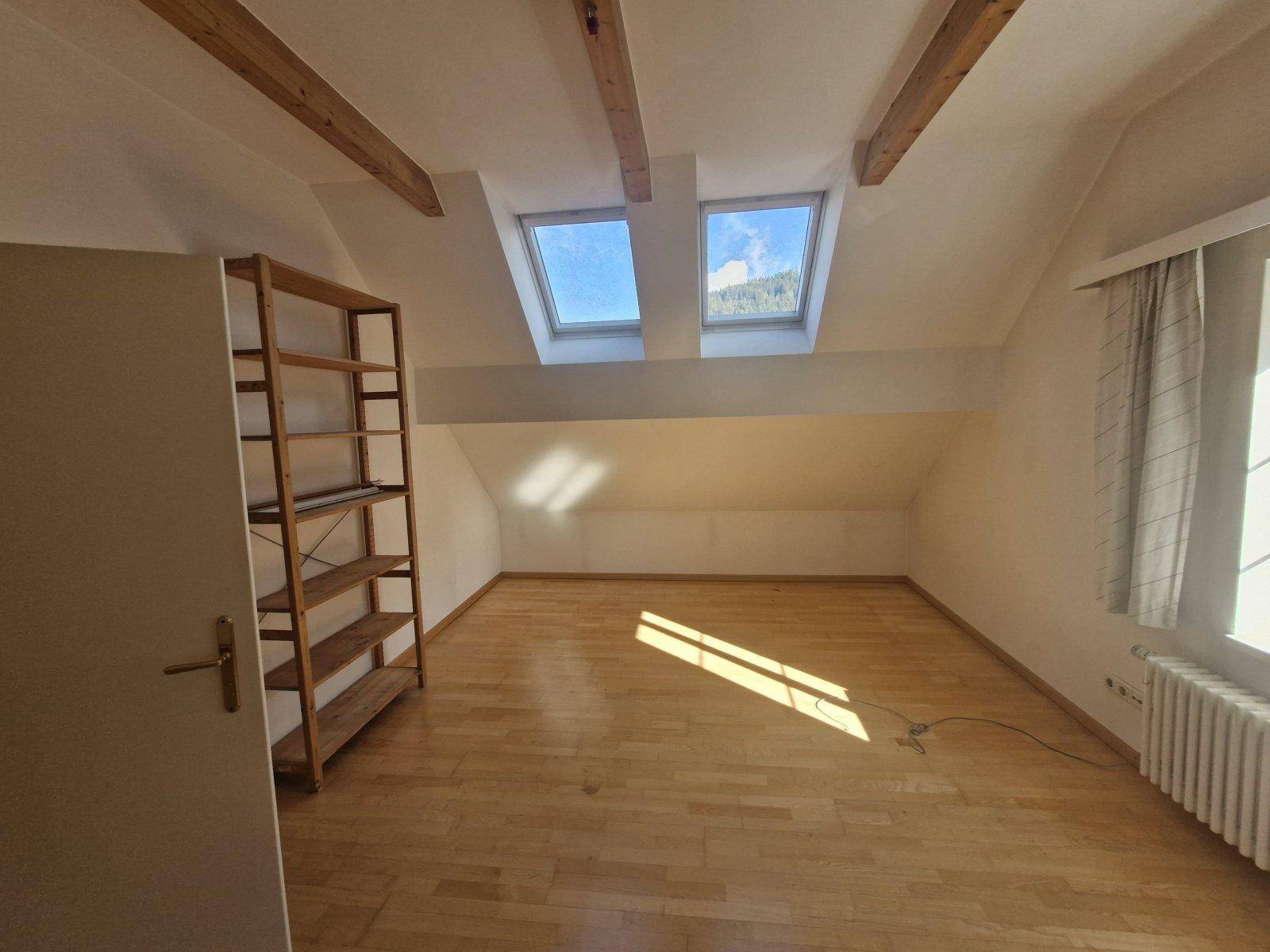 Helles Dachgeschosszimmer mit Holzbalken, Parkettboden und zwei Dachfenstern für viel Licht.