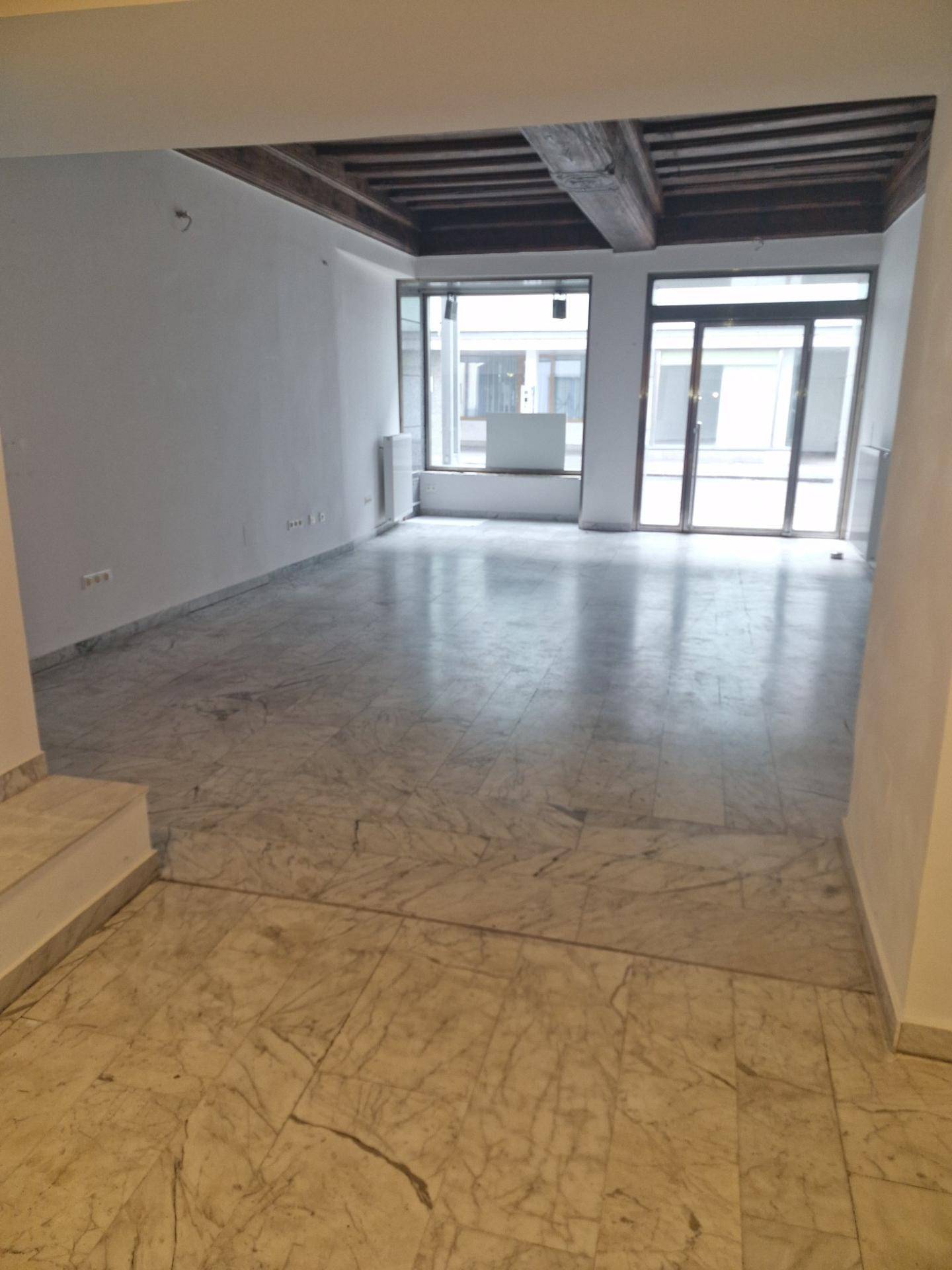 Heller Geschäftsraum mit Marmorboden, großen Schaufenstern und sichtbaren Holzdeckenbalken.