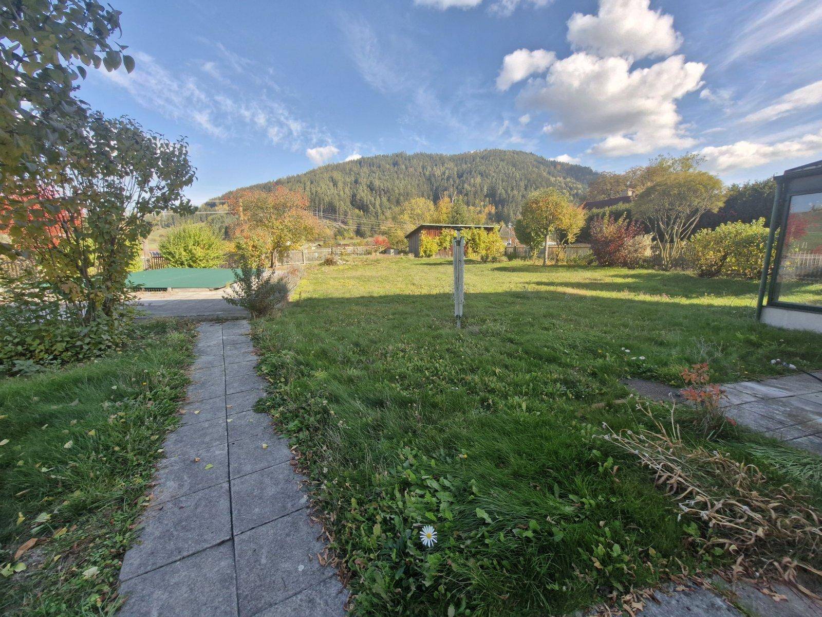Gepflasterter Weg führt durch den grünen Rasen des Gartens mit Bergblick.