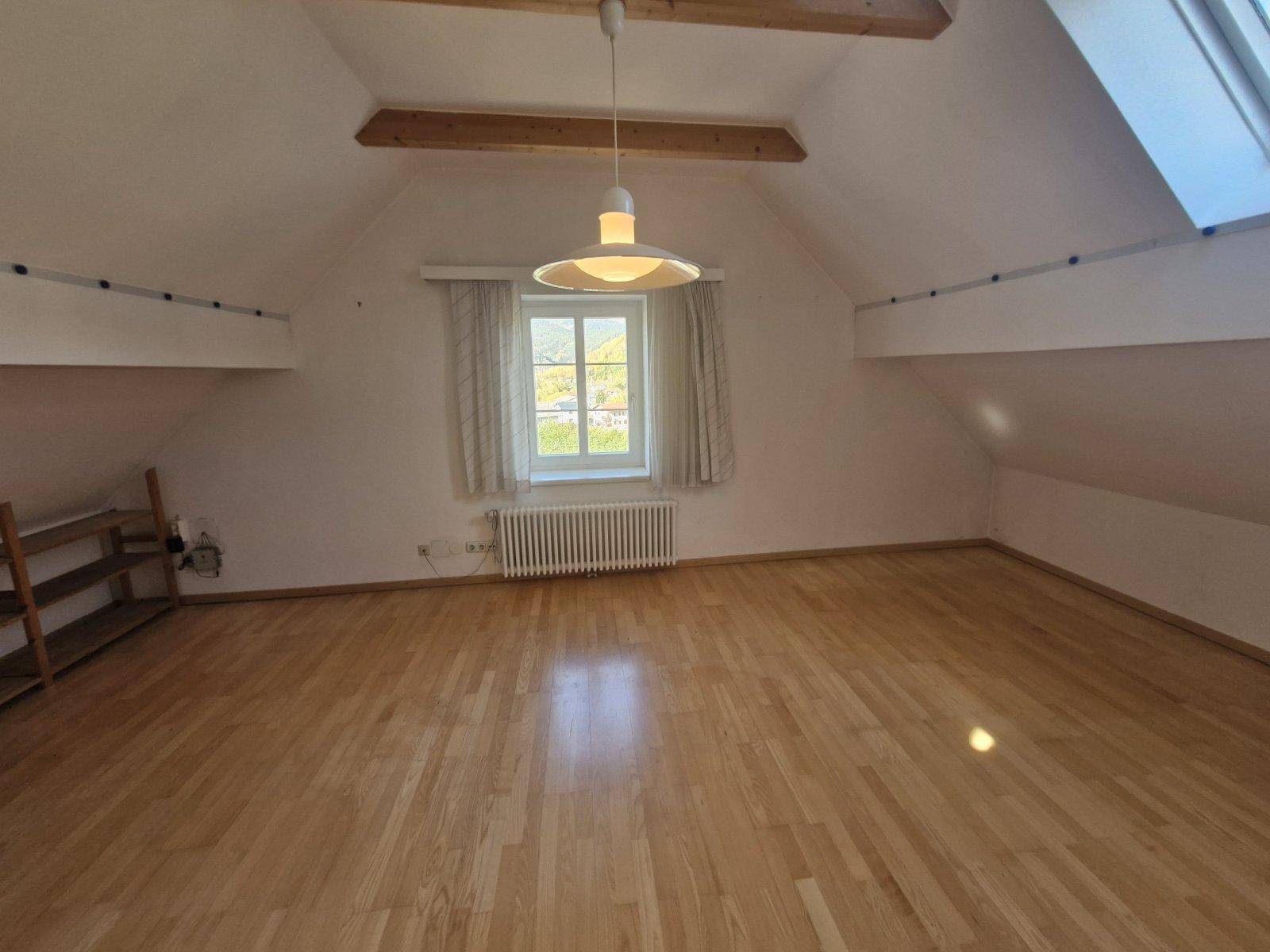 Geräumiges Dachgeschosszimmer mit Holzbalken, Parkettboden und einem Fenster mit Ausblick.
