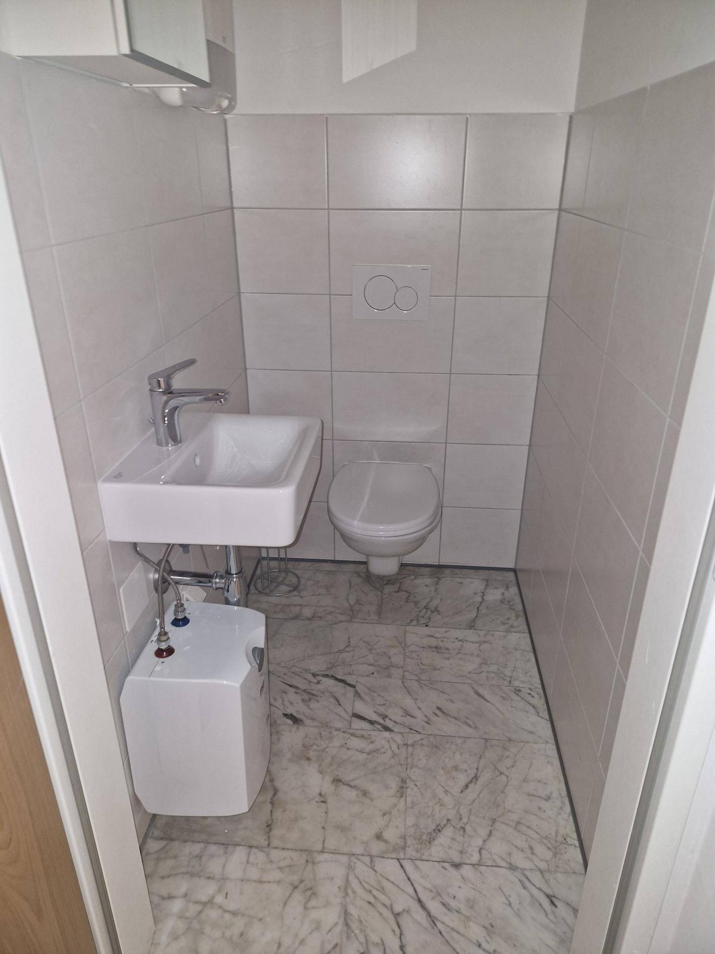 Kleine, geflieste Gästetoilette mit wandmontierter Toilette und modernem Waschbecken.