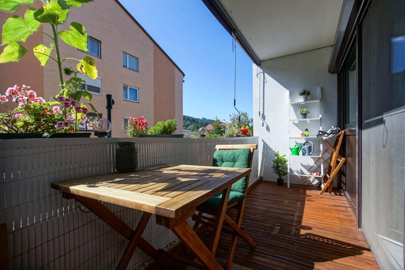 Sonniger Balkon mit Holzfußboden, Esstisch und Pflanzen, ideal für entspannte Stunden im Freien.
