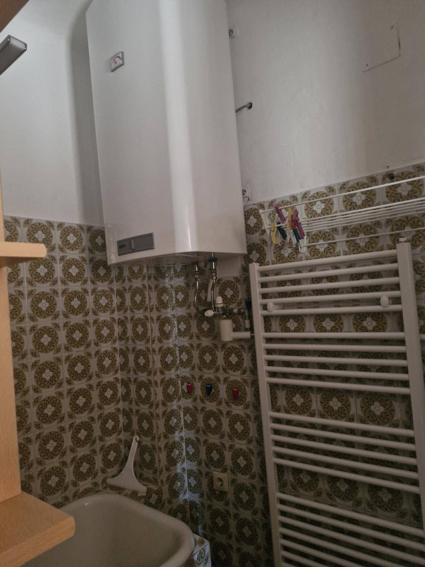 Badezimmer mit gemusterten Fliesen, Badewanne und Warmwasserboiler, ausgestattet mit Handtuchheizkörper.