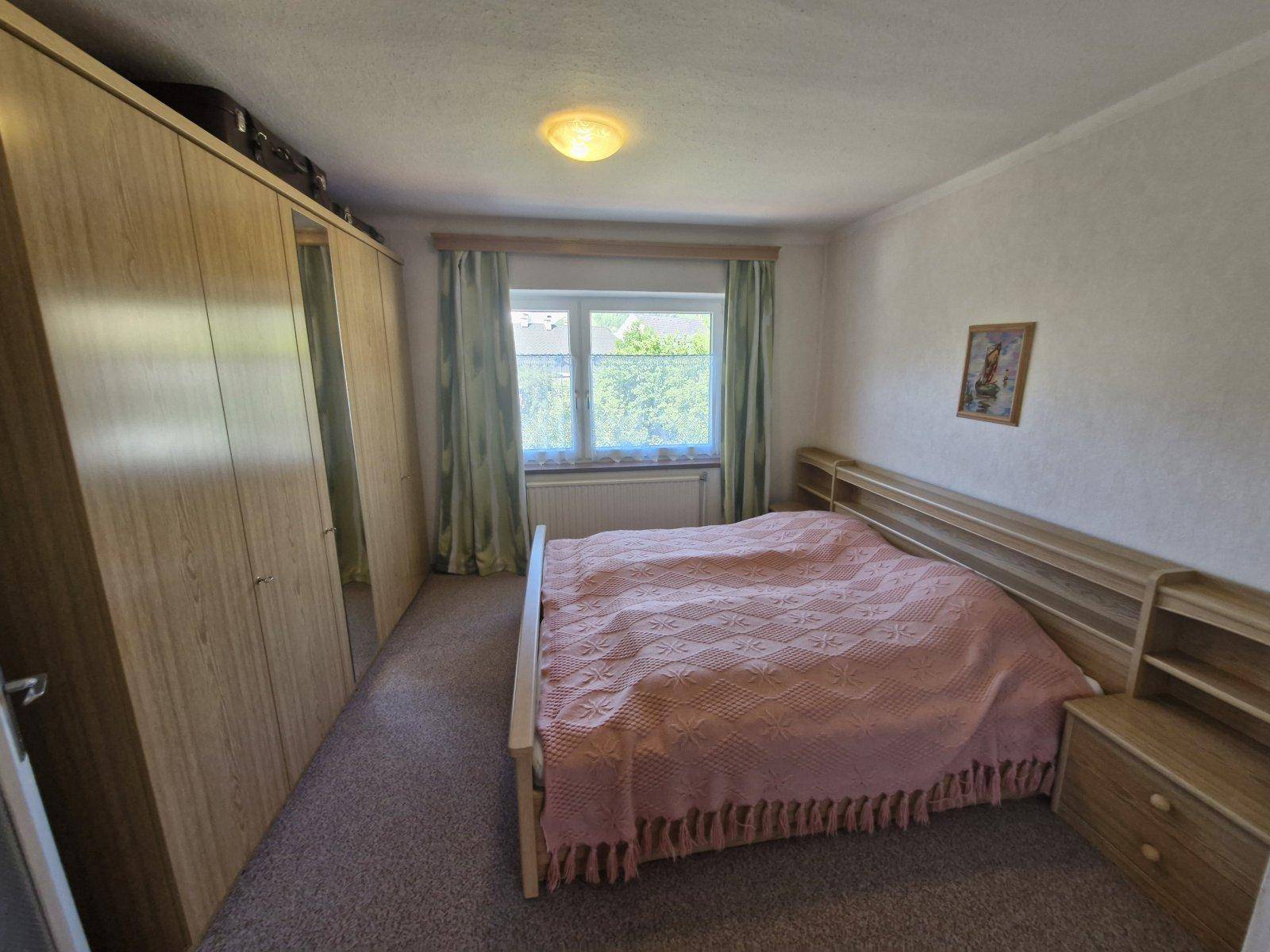 Schlafzimmer mit Doppelbett, großem Kleiderschrank und Fenster mit Blick ins Grüne.