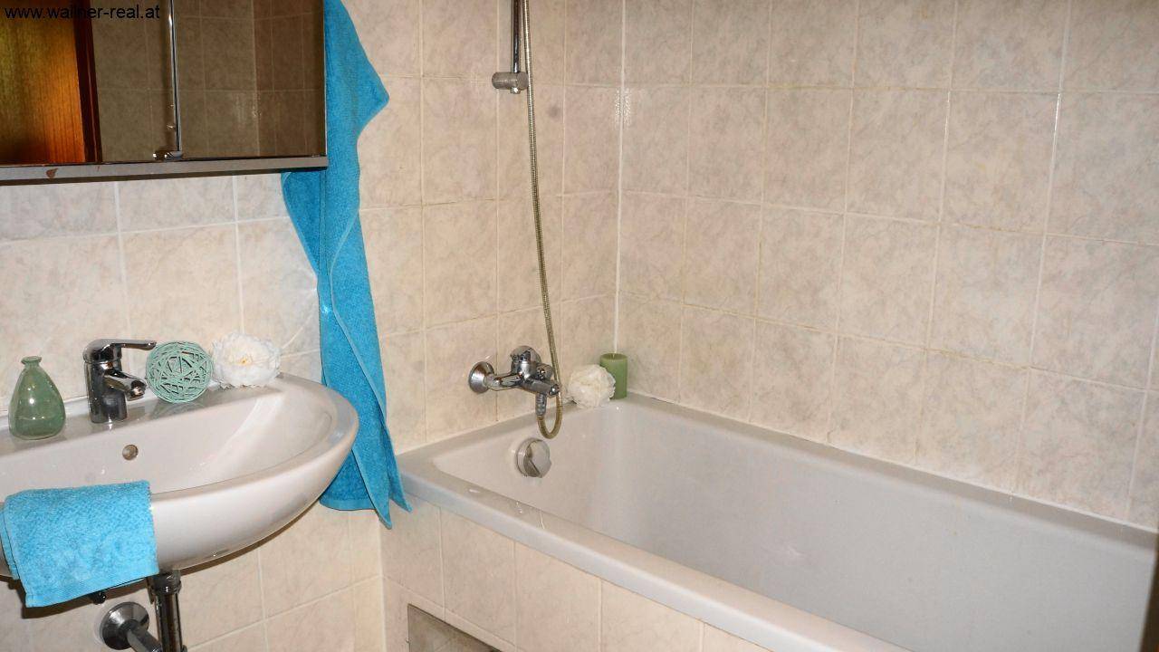 Badezimmer mit hellen Fliesen, Badewanne mit Duschfunktion und Waschbecken.