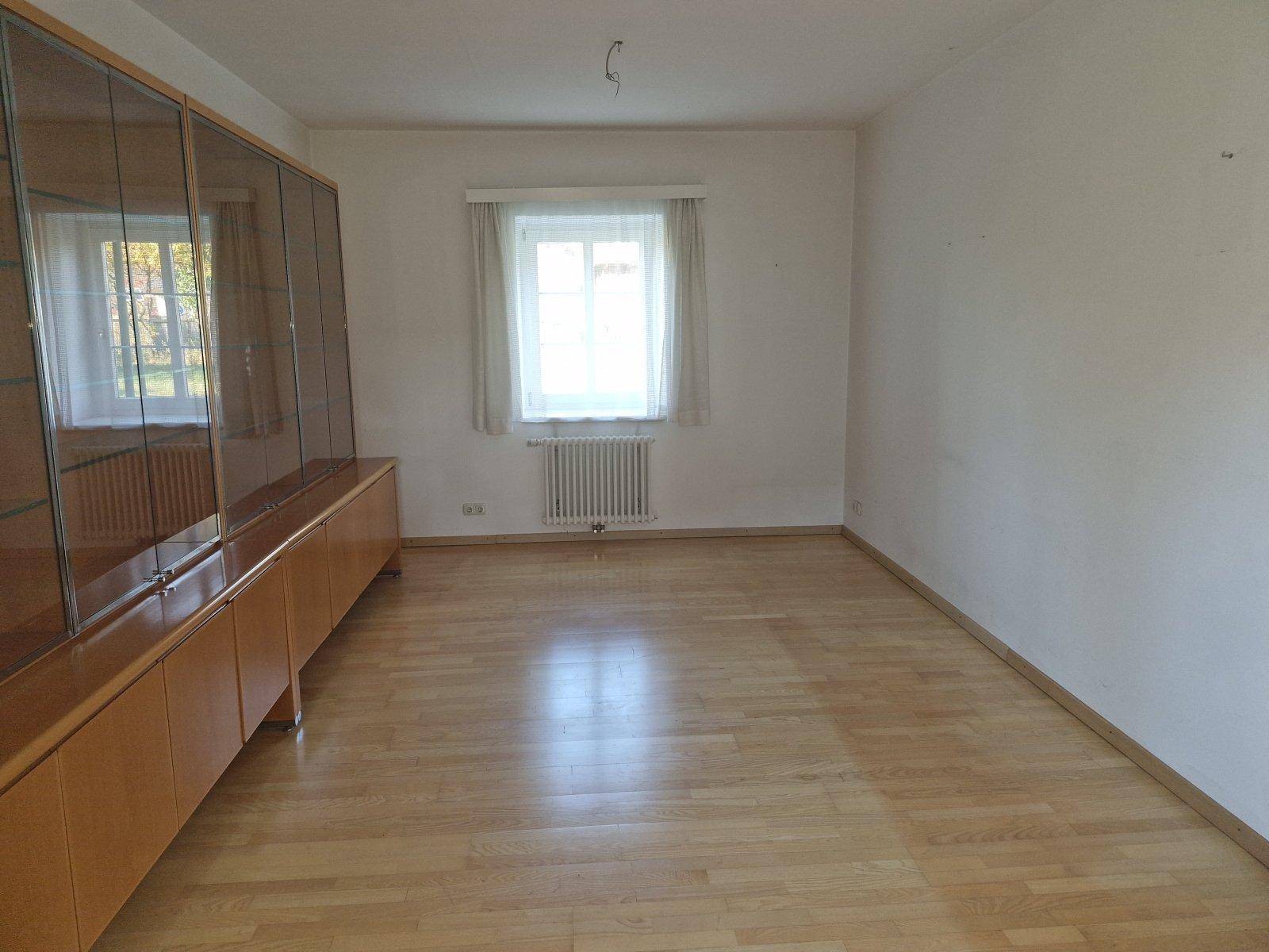 Helles Zimmer mit Parkettboden und einer langen Holzvitrine, ideal für Wohn- oder Essbereich.