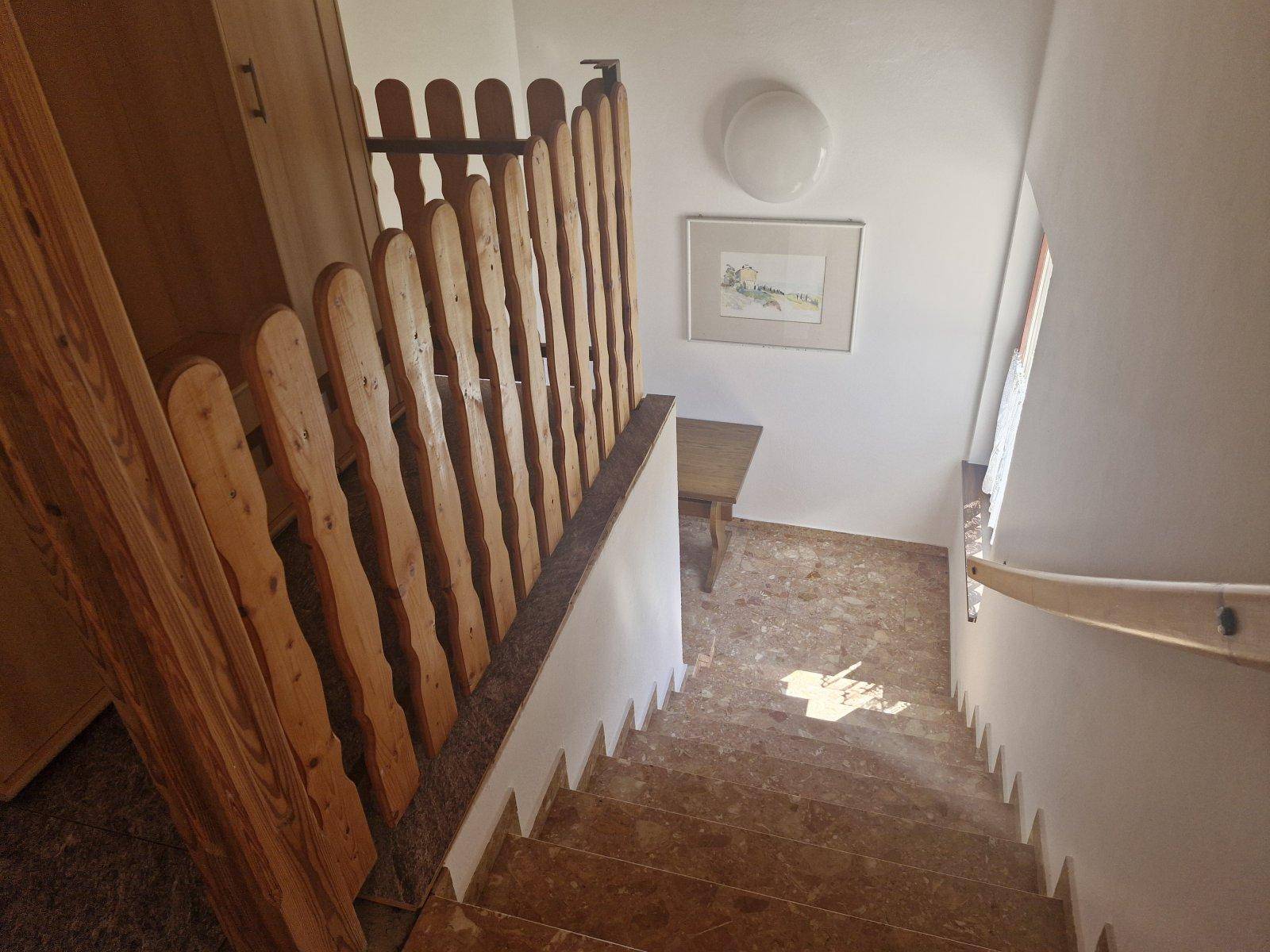 Treppenhaus mit Holzgeländer und gefliestem Boden, das die Etagen verbindet.