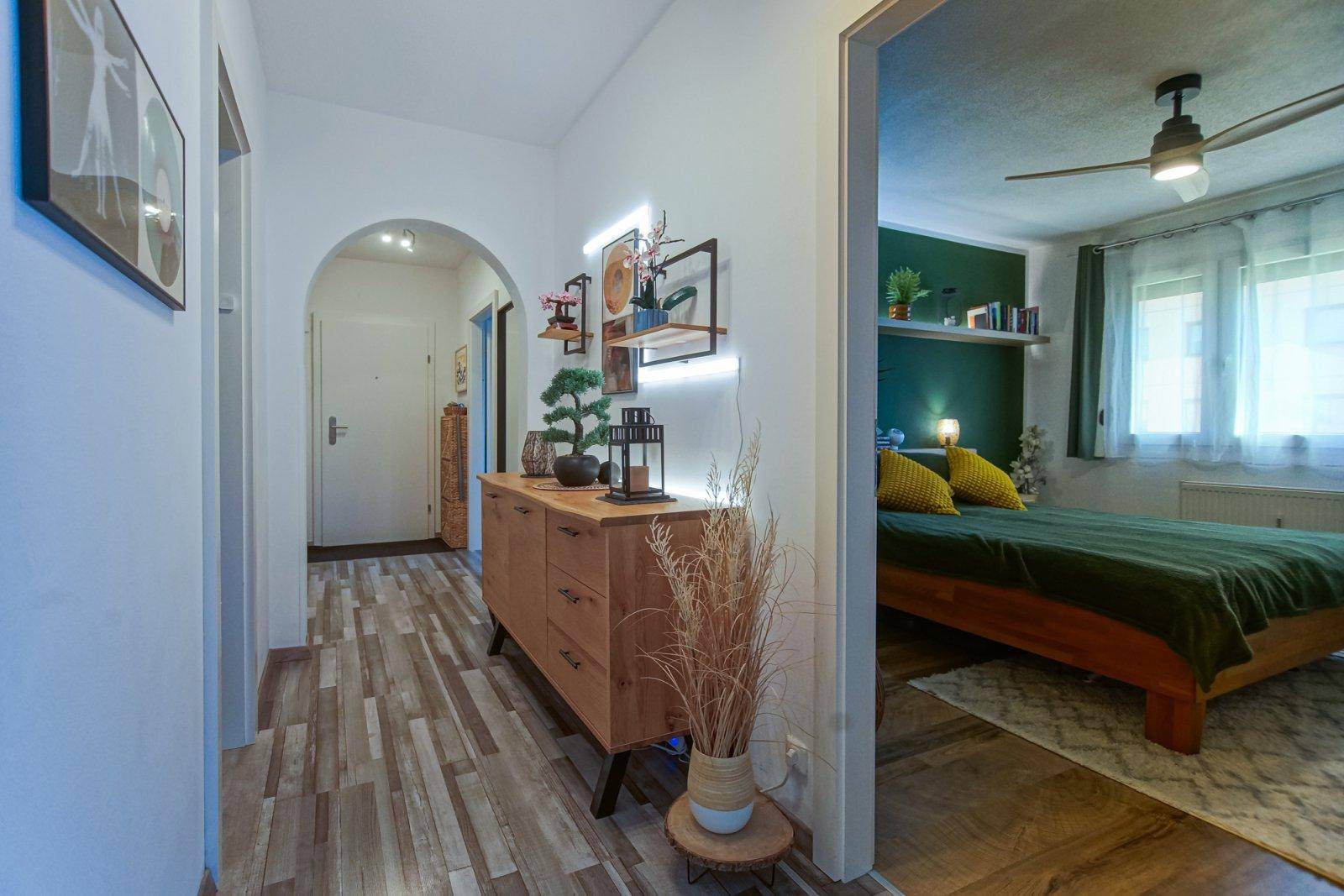 Heller Flur mit Holzkommode und offenem Zugang zu einem gemütlichen Schlafzimmer.
