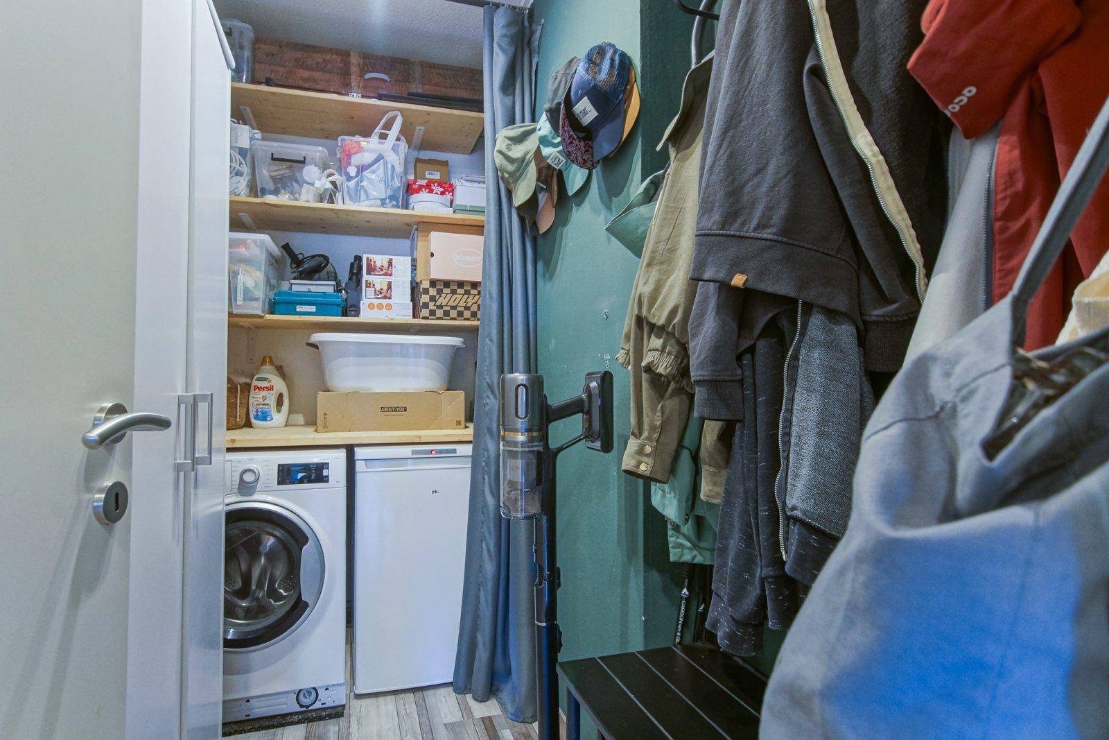 Praktischer Hauswirtschaftsraum mit Waschmaschine, Regalen und Stauraum für Kleidung.