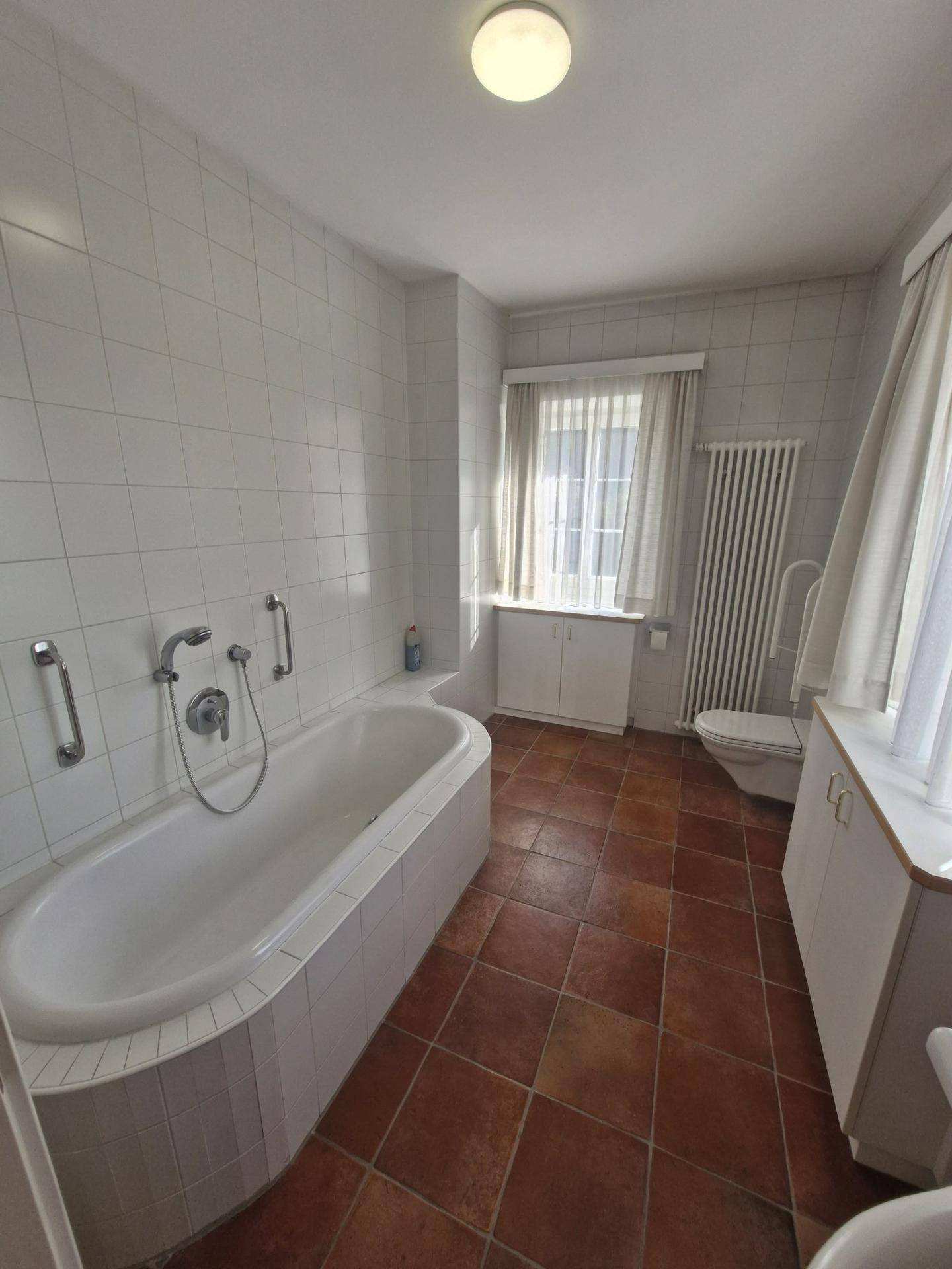 Geräumiges Badezimmer mit Badewanne, WC und Terrakottafliesen, ausgestattet mit Haltegriffen.