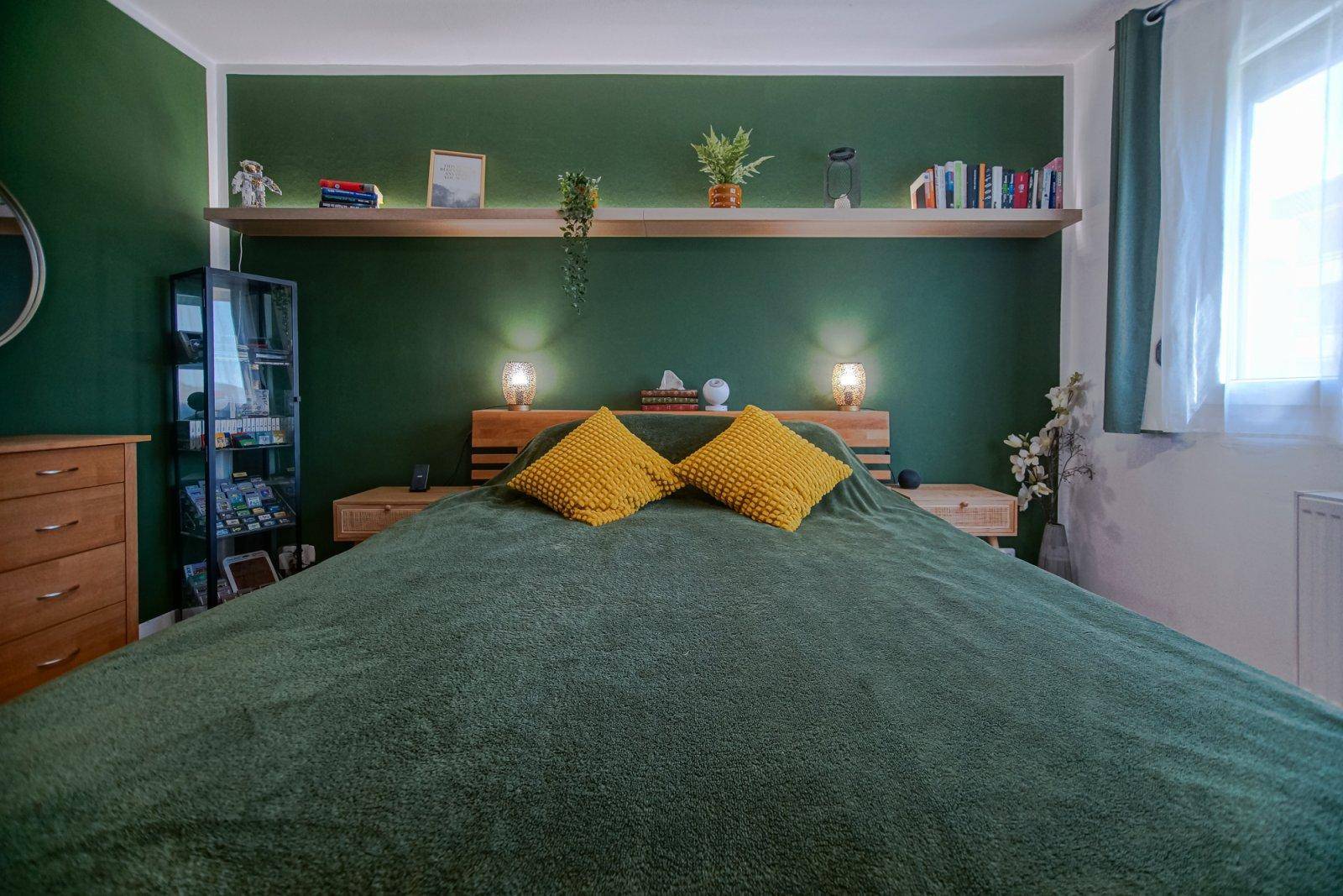Schlafzimmer mit Holzbett, grüner Akzentwand und dekorativem Regal über dem Bett.