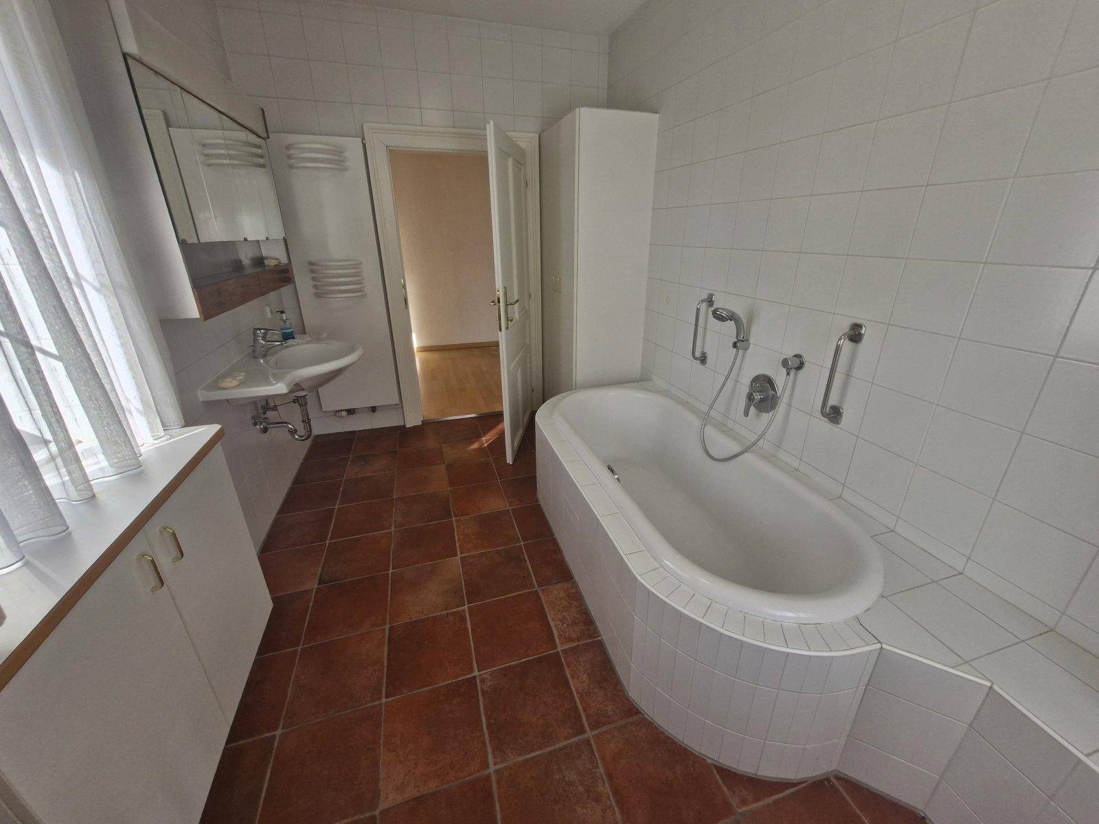 Badezimmer mit Badewanne, Waschbecken und Terrakottafliesen, bietet Zugang zu einem weiteren Raum.
