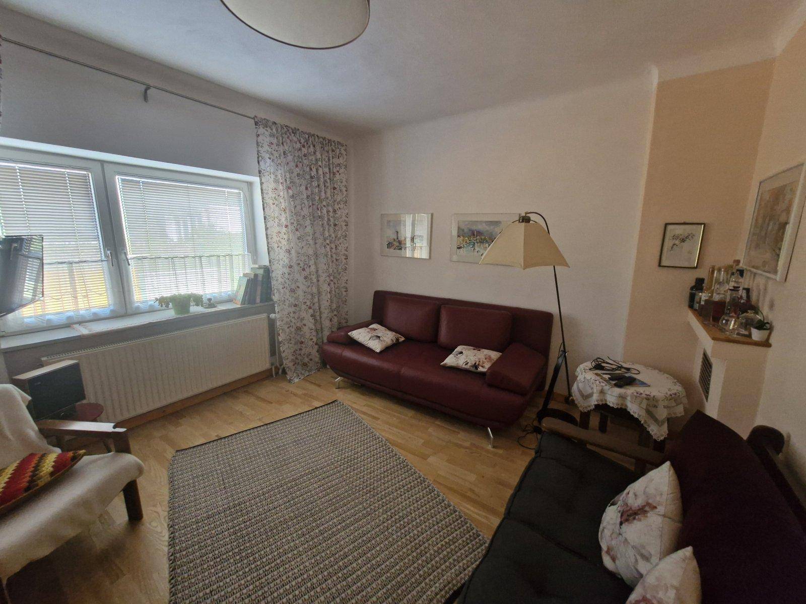 Gemütliches Wohnzimmer mit zwei Sofas, Stehlampe und Fenster mit Jalousien.