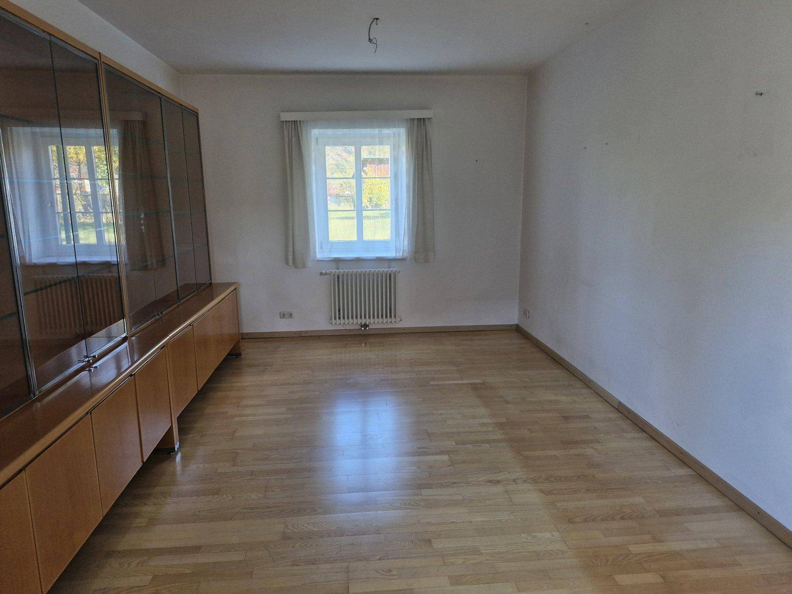Heller Raum mit Parkettboden, großem Fenster und einem langen Sideboard.