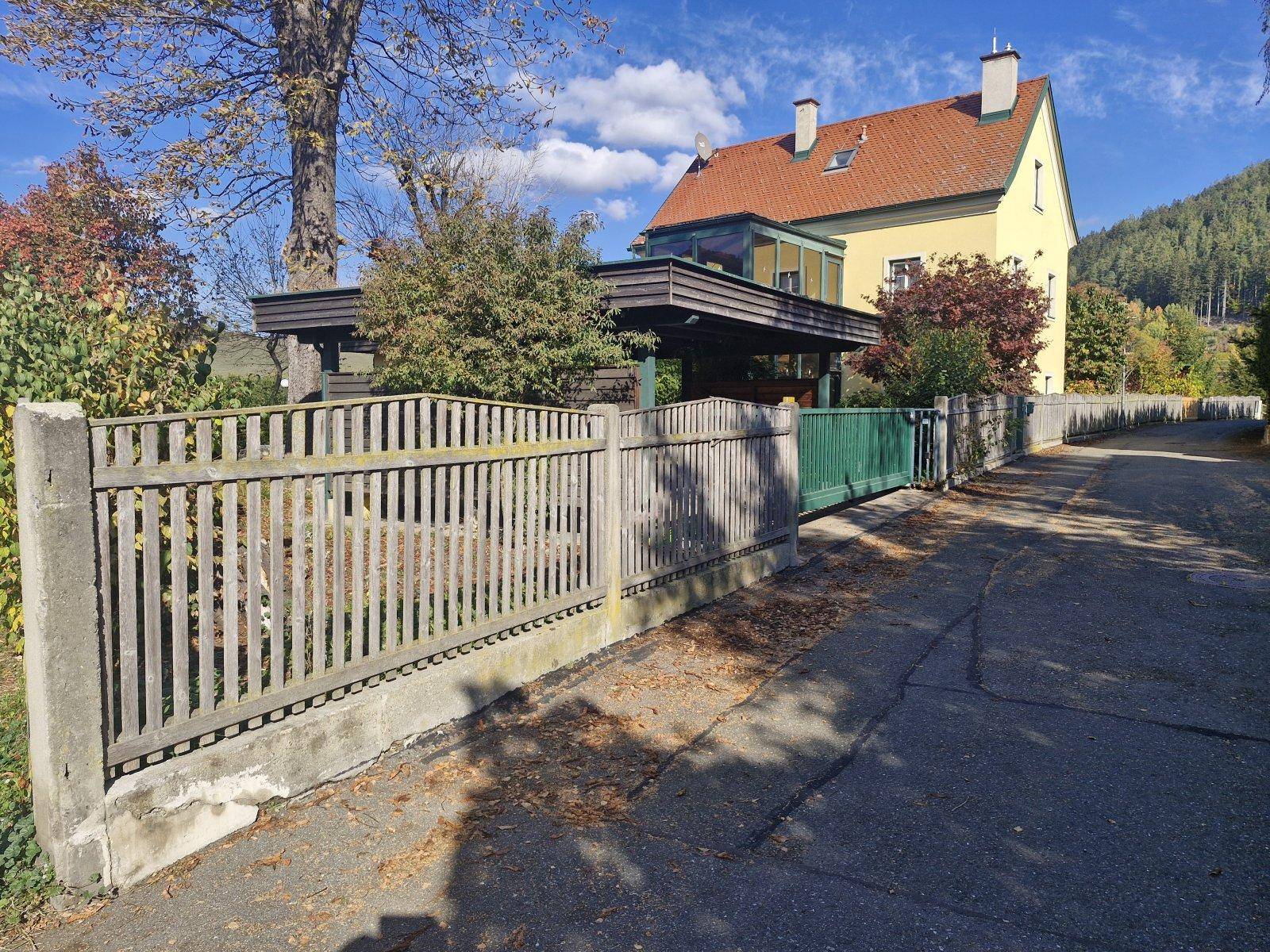 Blick auf das Haus von der Straße mit Holzzaun und überdachtem Carport.