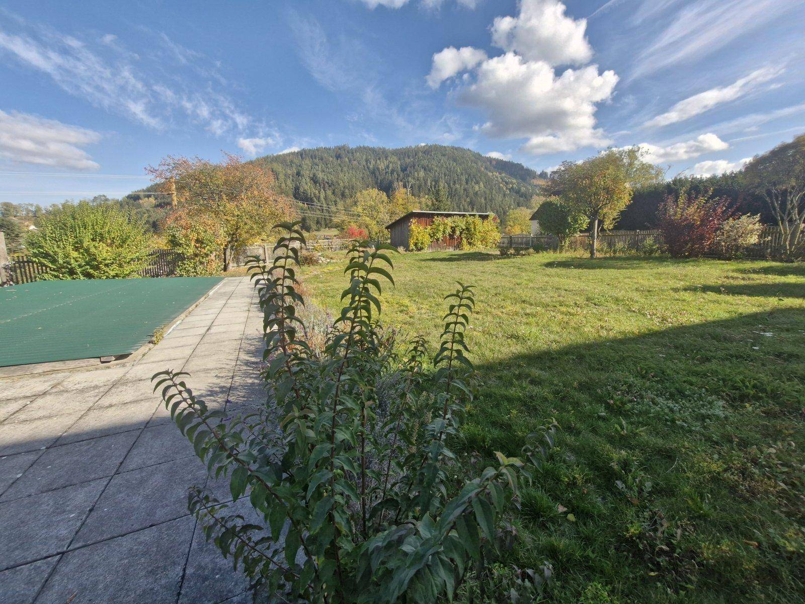 Gartenbereich mit gepflasterter Fläche, abgedecktem Pool und weitem Blick auf die Berge.