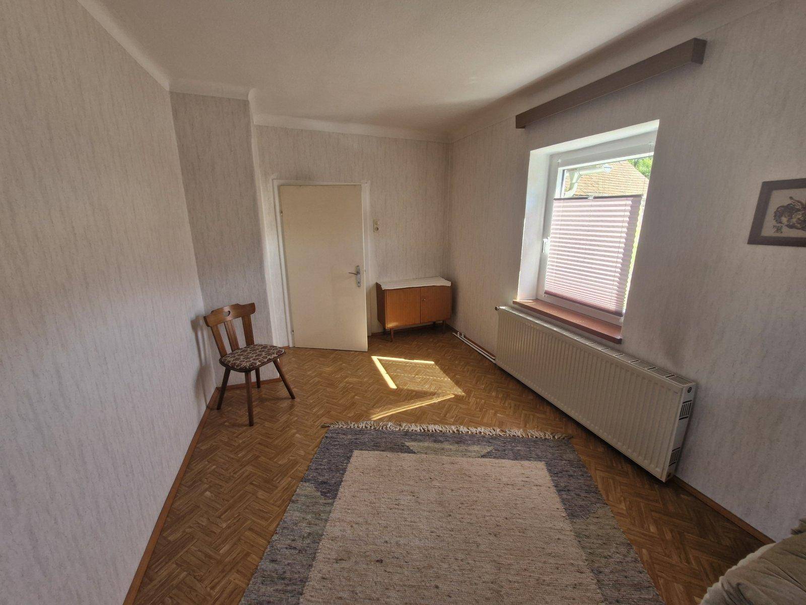 Helles Zimmer mit Parkettboden, Teppich und Fenster mit Jalousien für Privatsphäre.