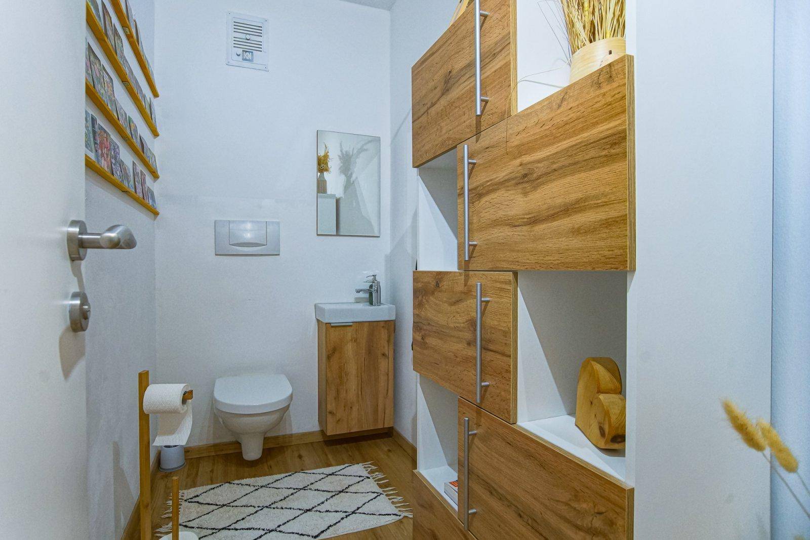 Modernes Gäste-WC mit wandhängender Toilette, kleinem Waschbecken und praktischen Holzregalen.