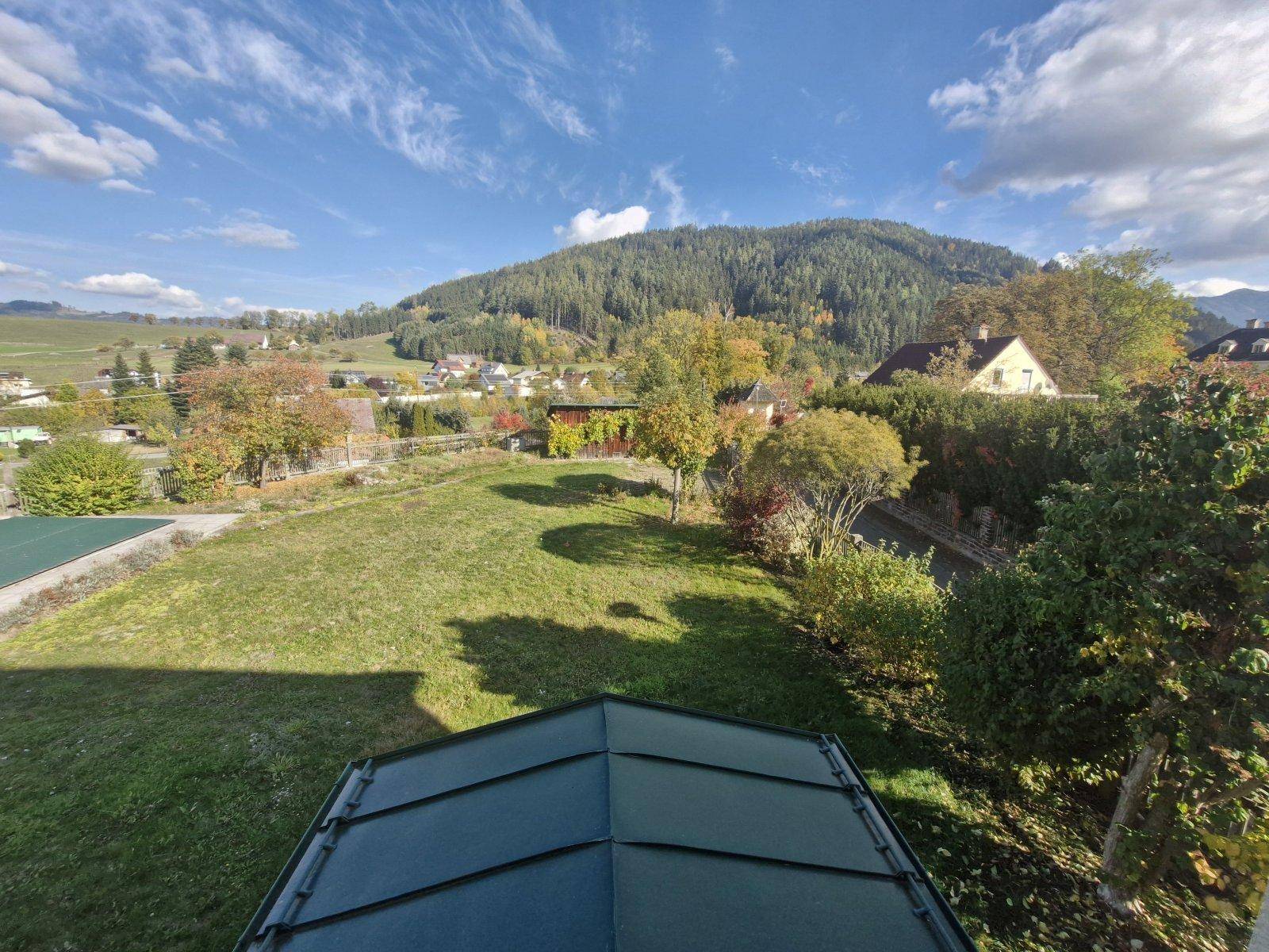 Panoramablick über den Garten und die bewaldeten Berge unter blauem Himmel.