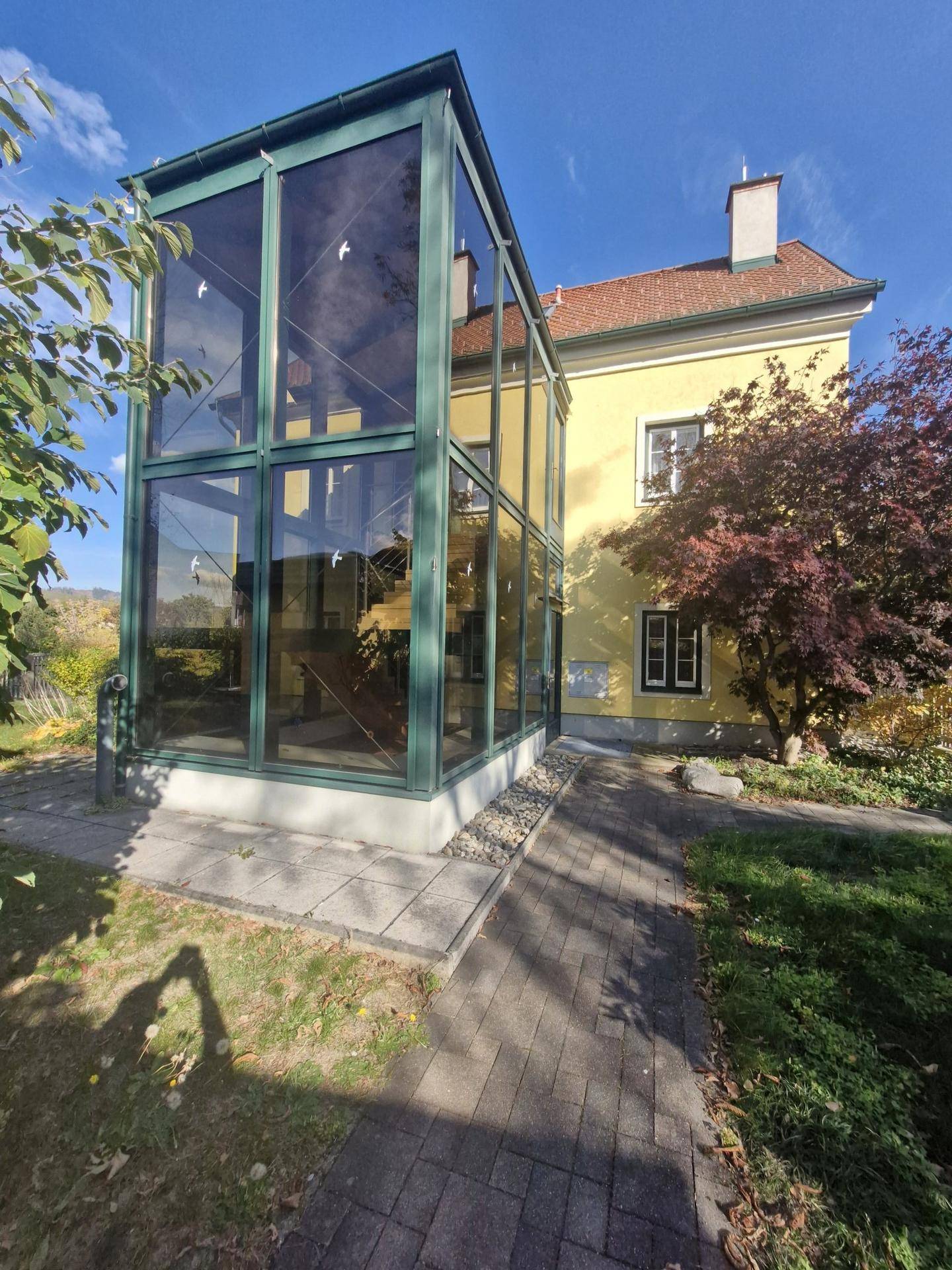 Nahaufnahme des modernen verglasten Wintergartens mit Zugang zum Haus und gepflastertem Weg.