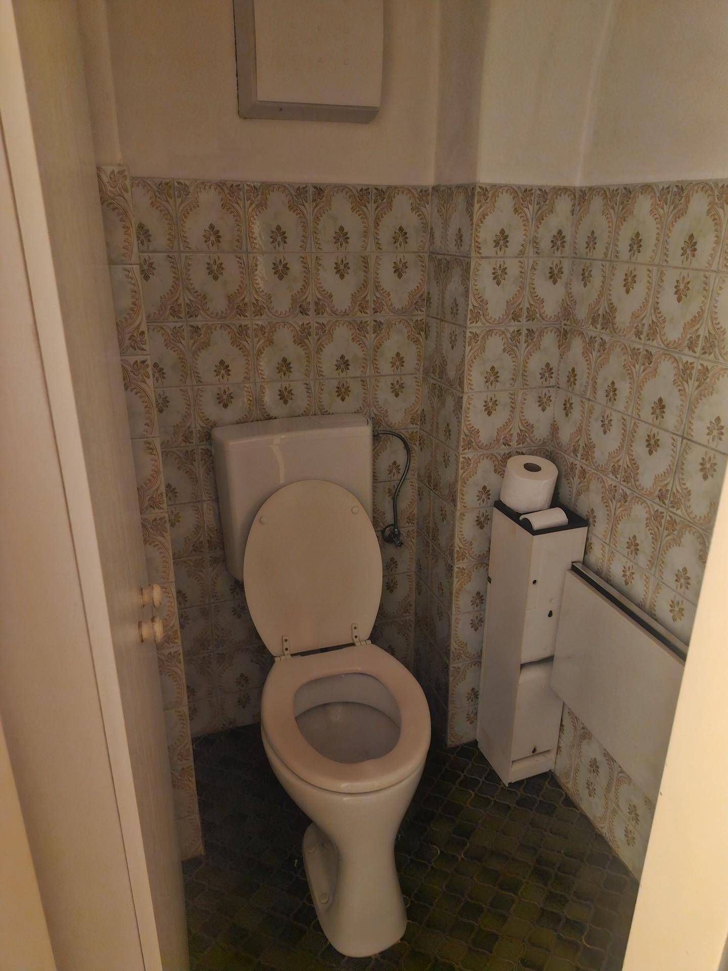 Kleine Toilette mit gemusterten Wandfliesen und einem Stand-WC, das einen funktionalen Raum bietet.