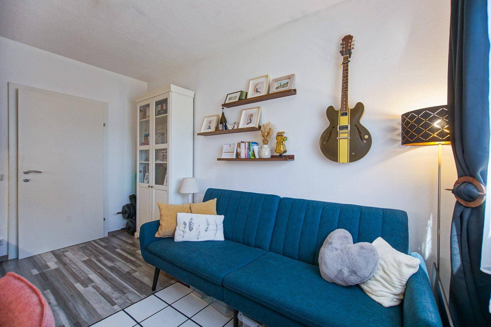 Vielseitiger Raum mit blauer Couch, Wandregalen und einer Gitarre als Dekoration.
