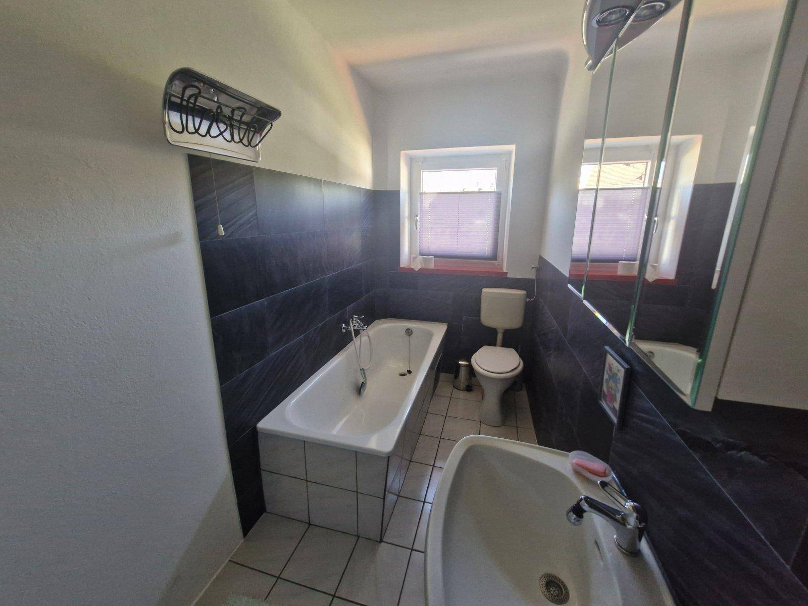 Modernisiertes Badezimmer mit Badewanne, Waschbecken und dunklen Wandfliesen.