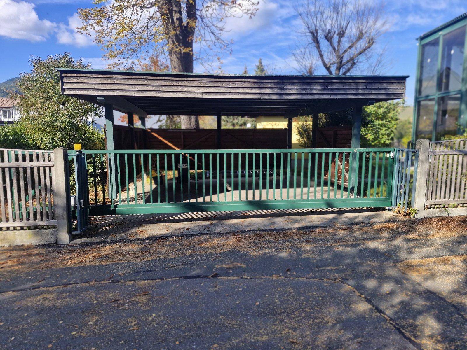 Einfahrt zum Grundstück mit grünem Schiebetor und überdachtem Carport.