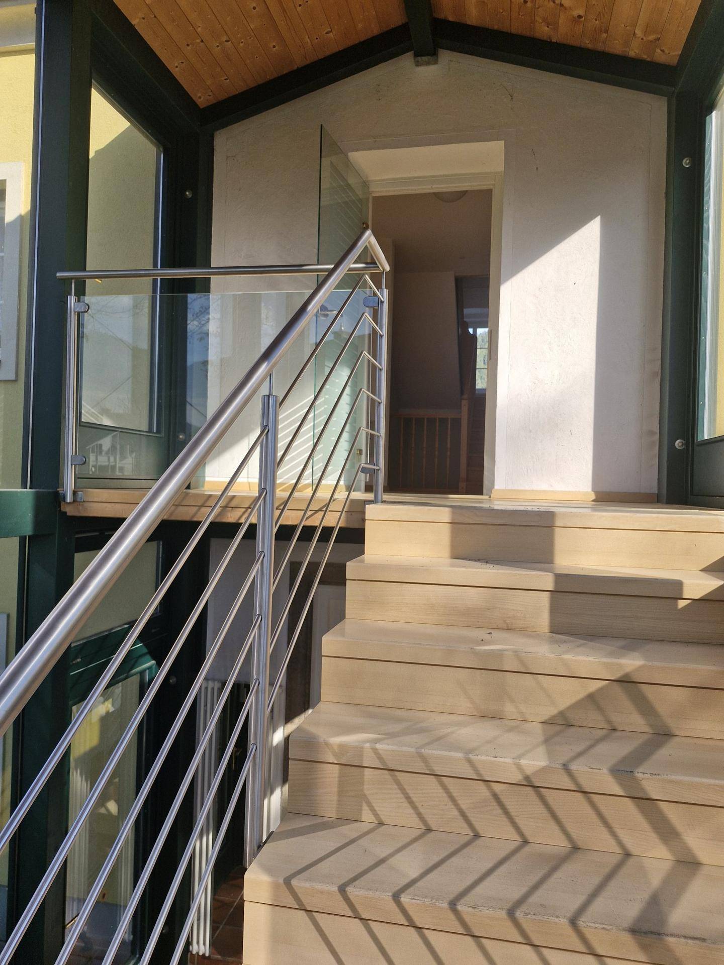 Heller Eingangsbereich im verglasten Anbau mit moderner Treppe und Edelstahlgeländer.