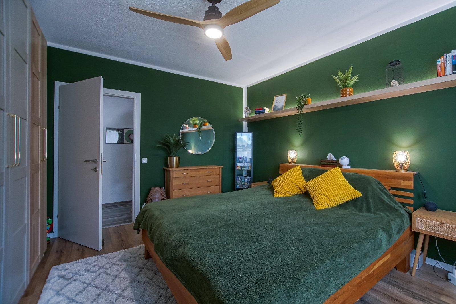 Helles Schlafzimmer mit Holzbett, grüner Akzentwand, Deckenventilator und Einbauschränken.